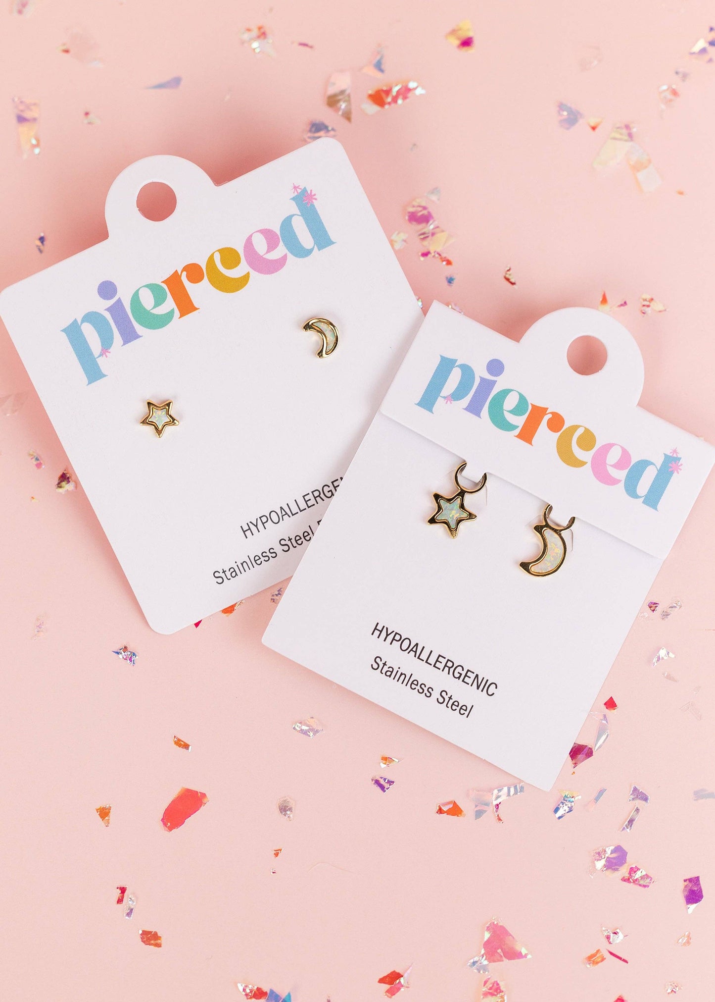 Two pairs of small gold-tone stud earrings on white display cards. One pair is a star and moon set, and the other is a crescent moon and star set.