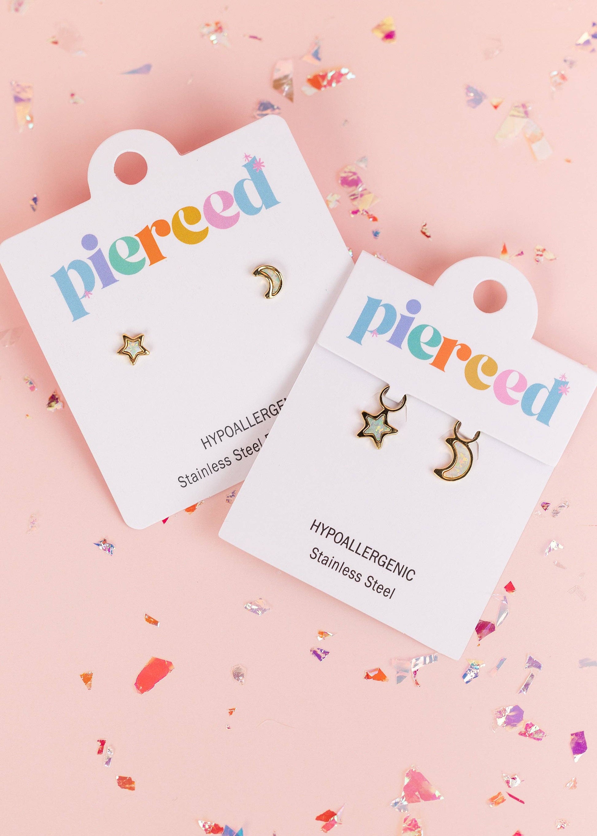 Two pairs of small gold-tone stud earrings on white display cards. One pair is a star and moon set, and the other is a crescent moon and star set.