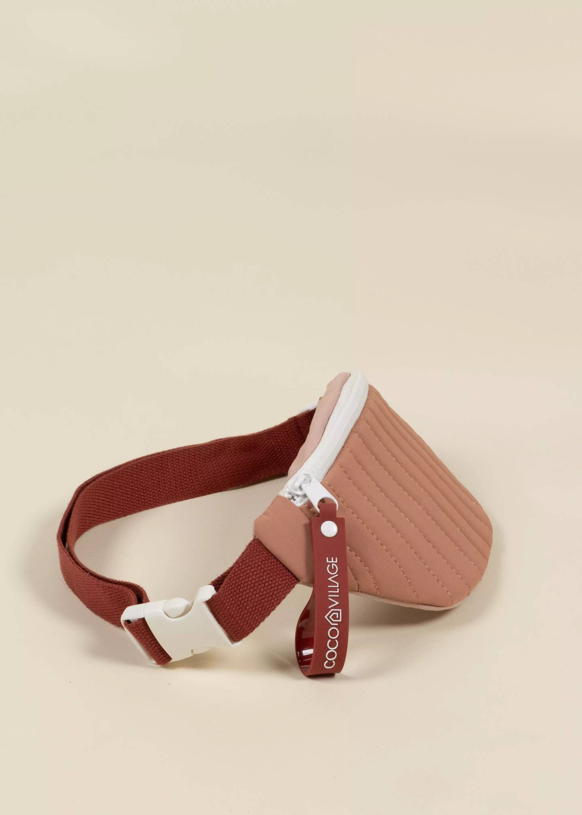 Brown quilted waist bag with a white zipper on a beige background