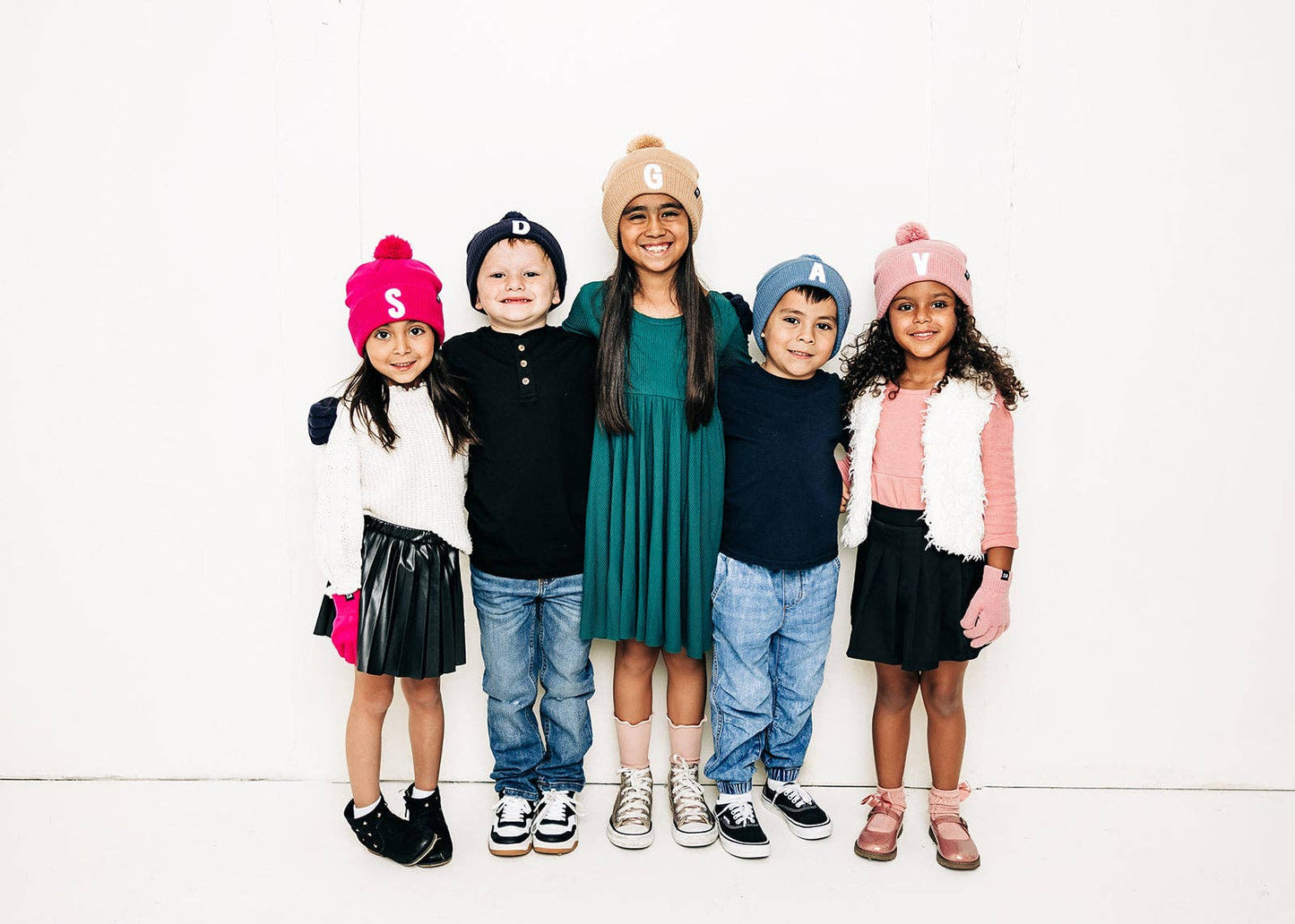 Five children wearing colorful hats and clothing standing together on a white background