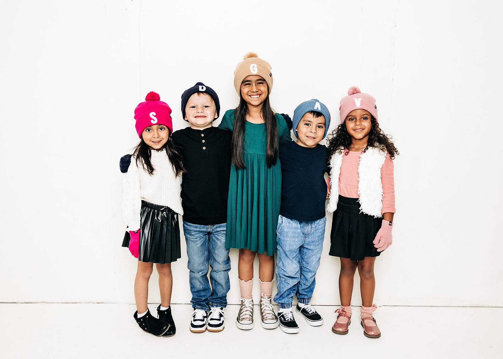 Five children wearing colorful hats and clothing standing together on a white background