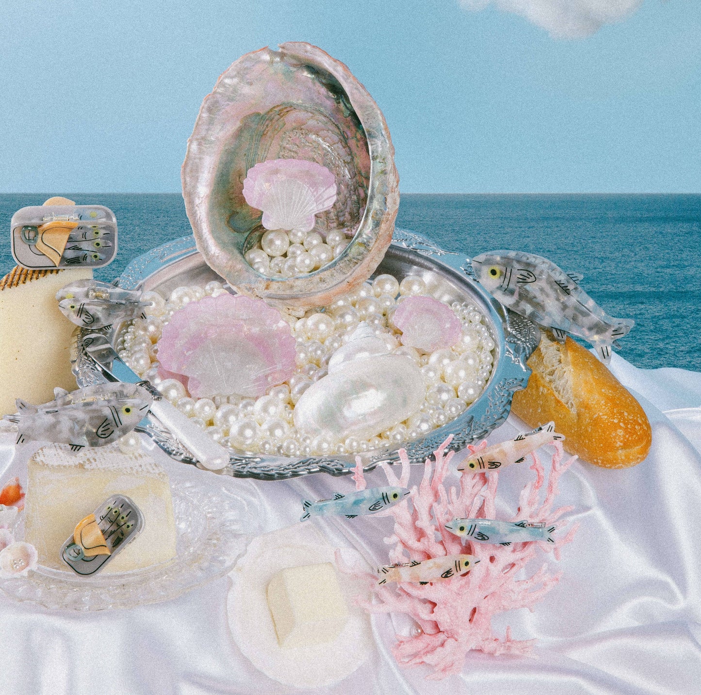 Seashell with pearls, coral, and small fish figurines on a white surface with ocean background
