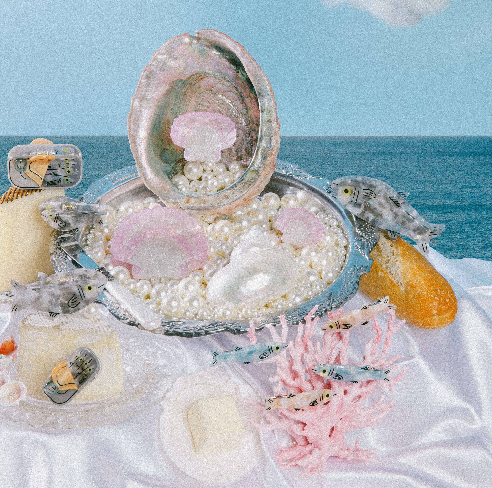 Seashell with pearls, coral, and small fish figurines on a white surface with ocean background