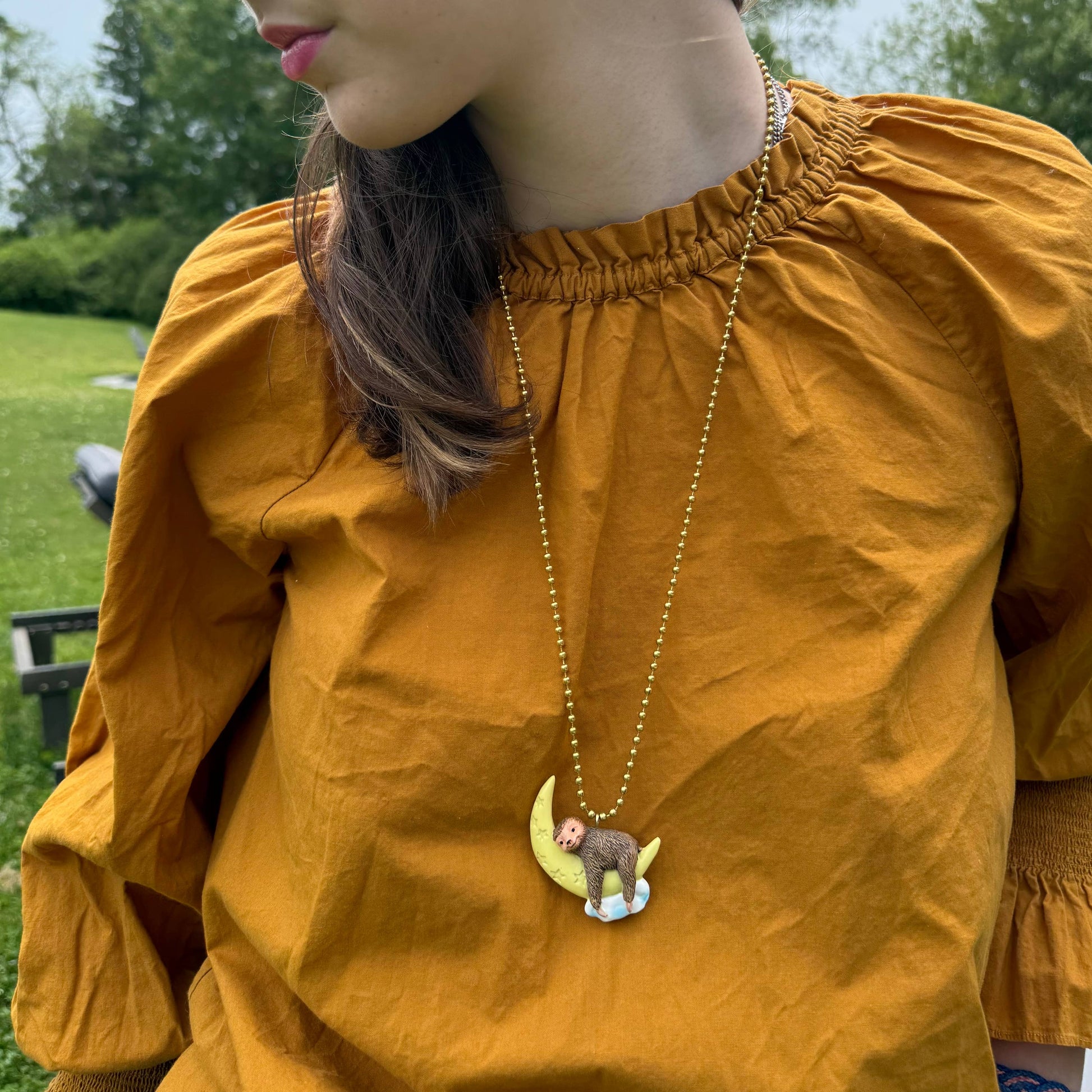 Person wearing a mustard yellow top with a necklace featuring a moon and star pendant outdoors.