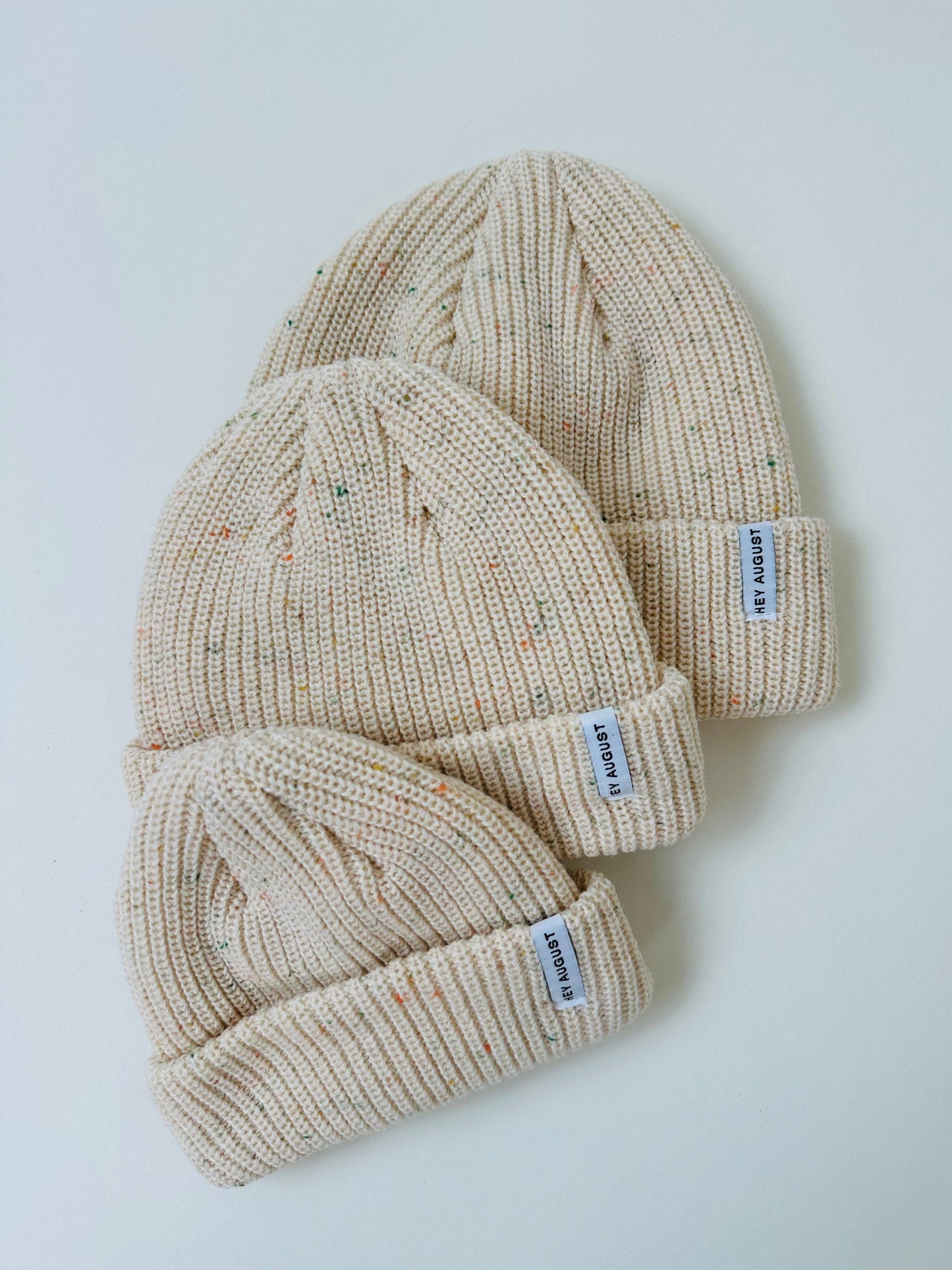 Three beige knit hats stacked on a light gray background