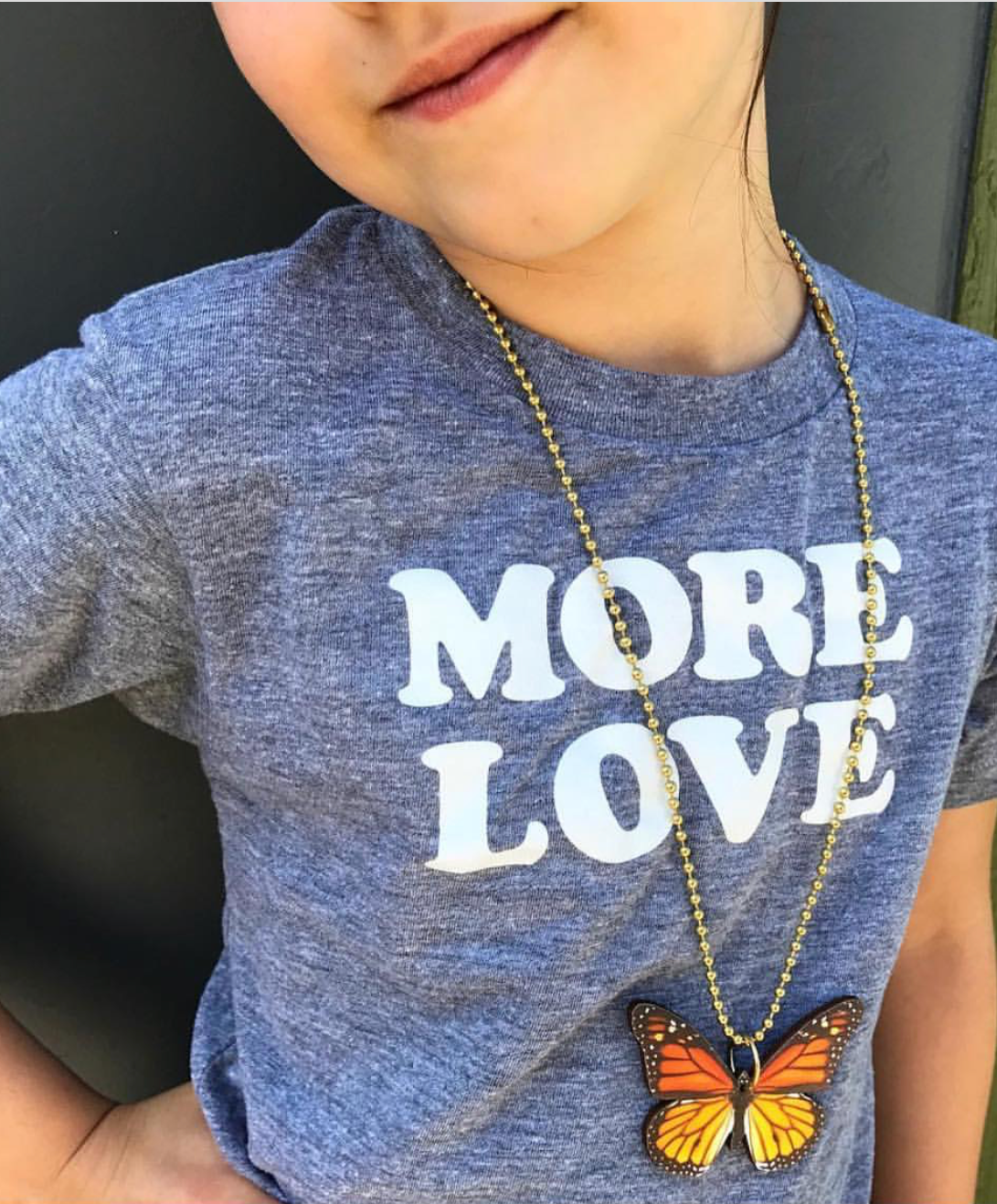 Child wearing a blue shirt with 'MORE LOVE' text and a butterfly necklace.