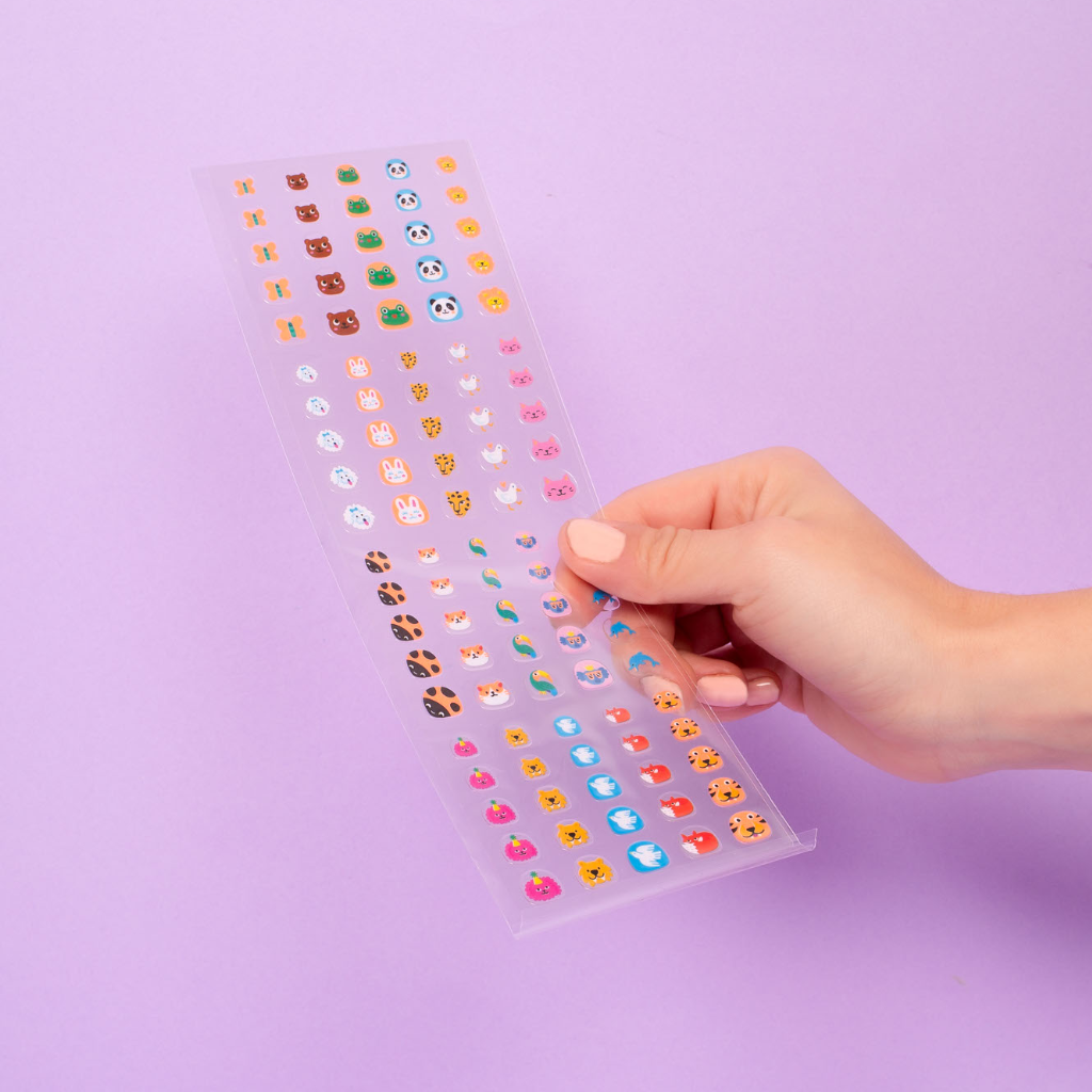 Hand holding a clear sheet with colorful nail stickers against a purple background