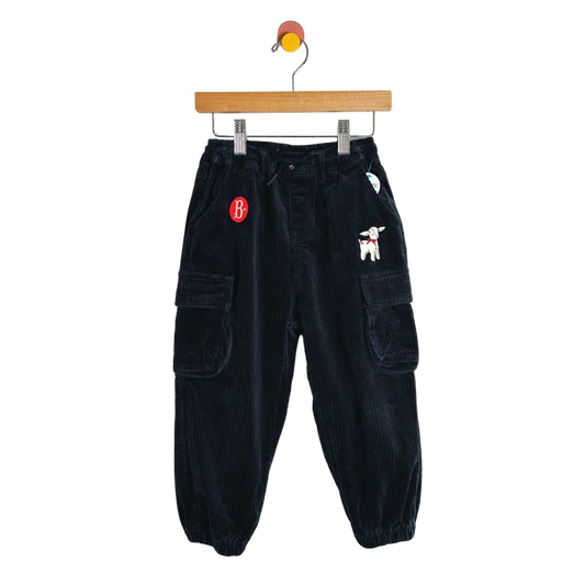 Black corduroy pants with patches on a hanger against a white background