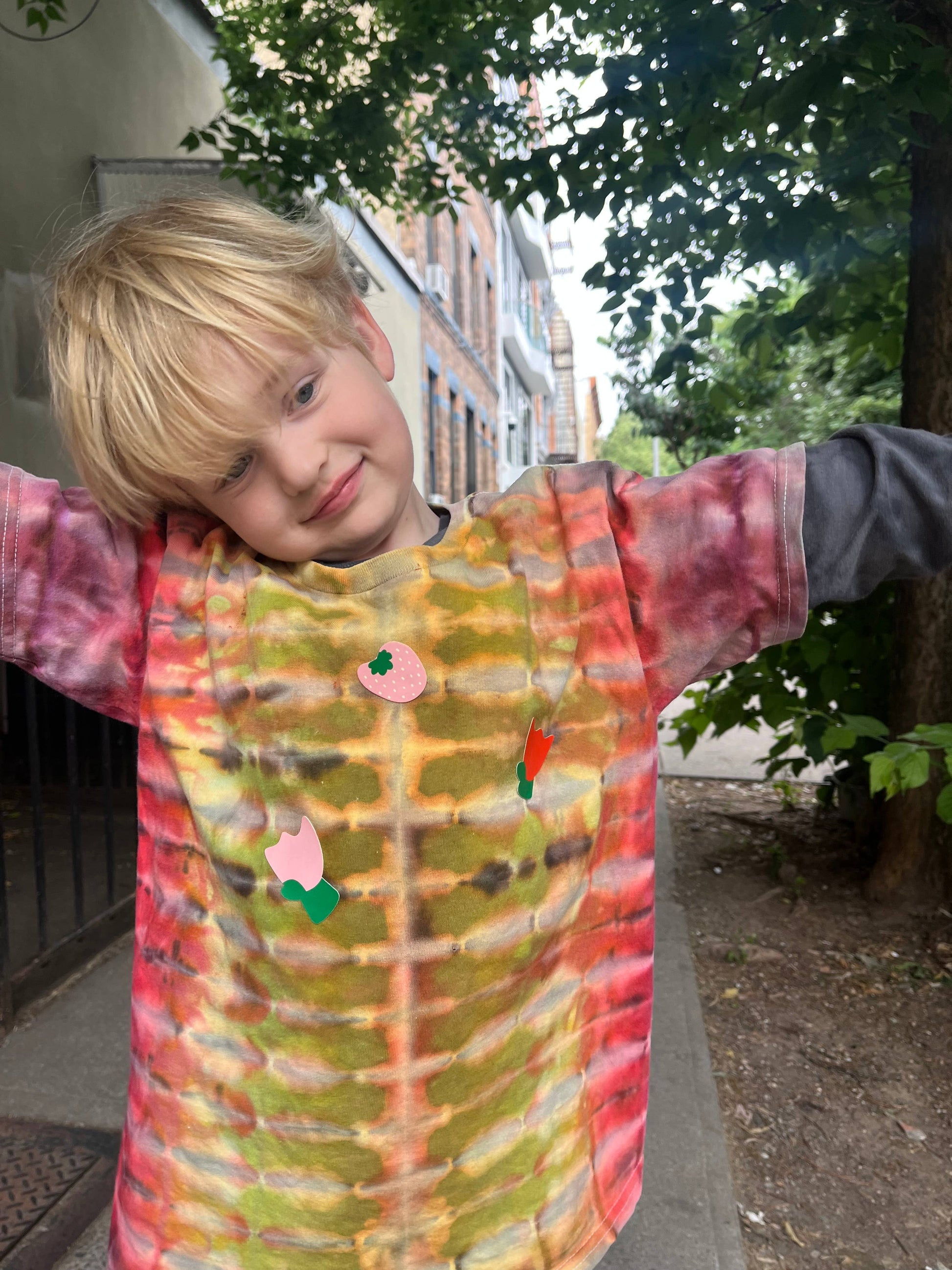 Child wearing a colorful tie-dye shirt with patches outdoors.