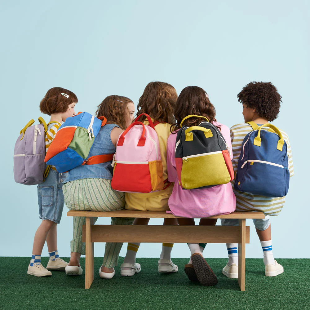 Children with colorful backpacks sitting on a bench against a light blue background