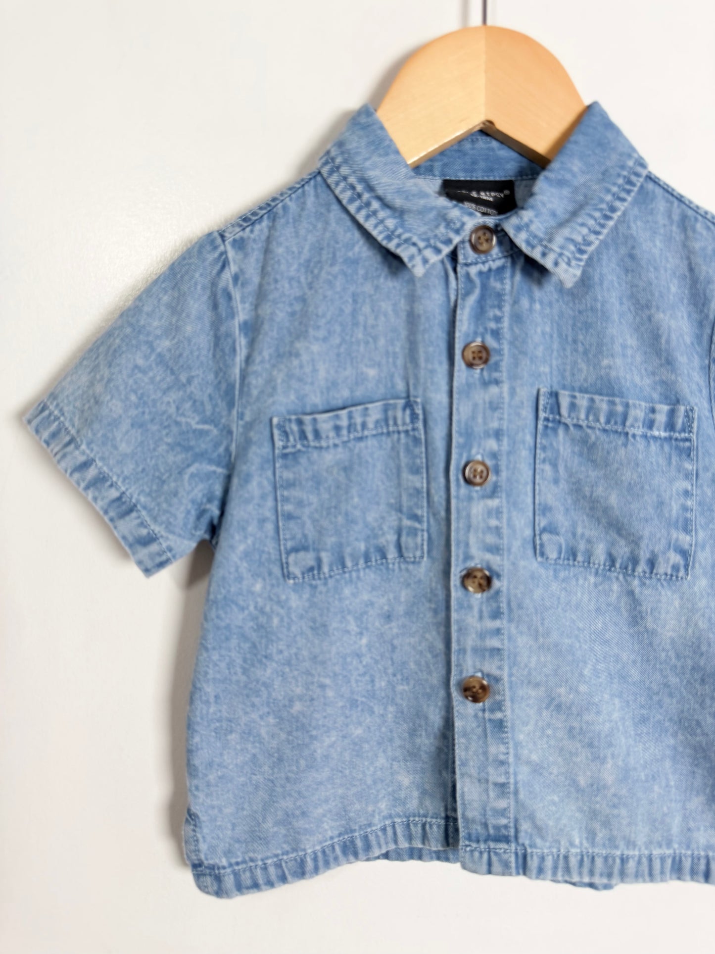 Blue denim shirt on a wooden hanger against a white background