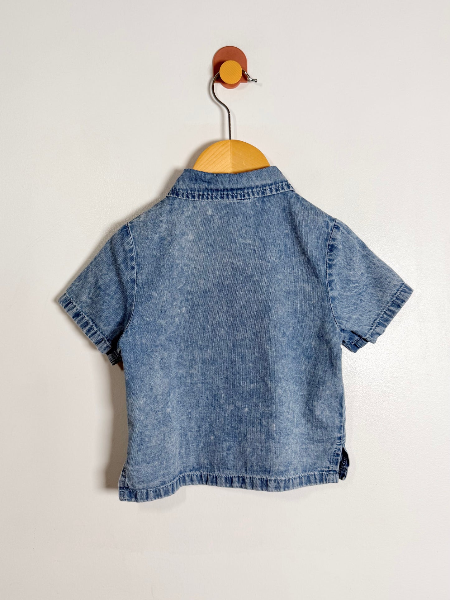 Blue denim shirt on a wooden hanger against a white background
