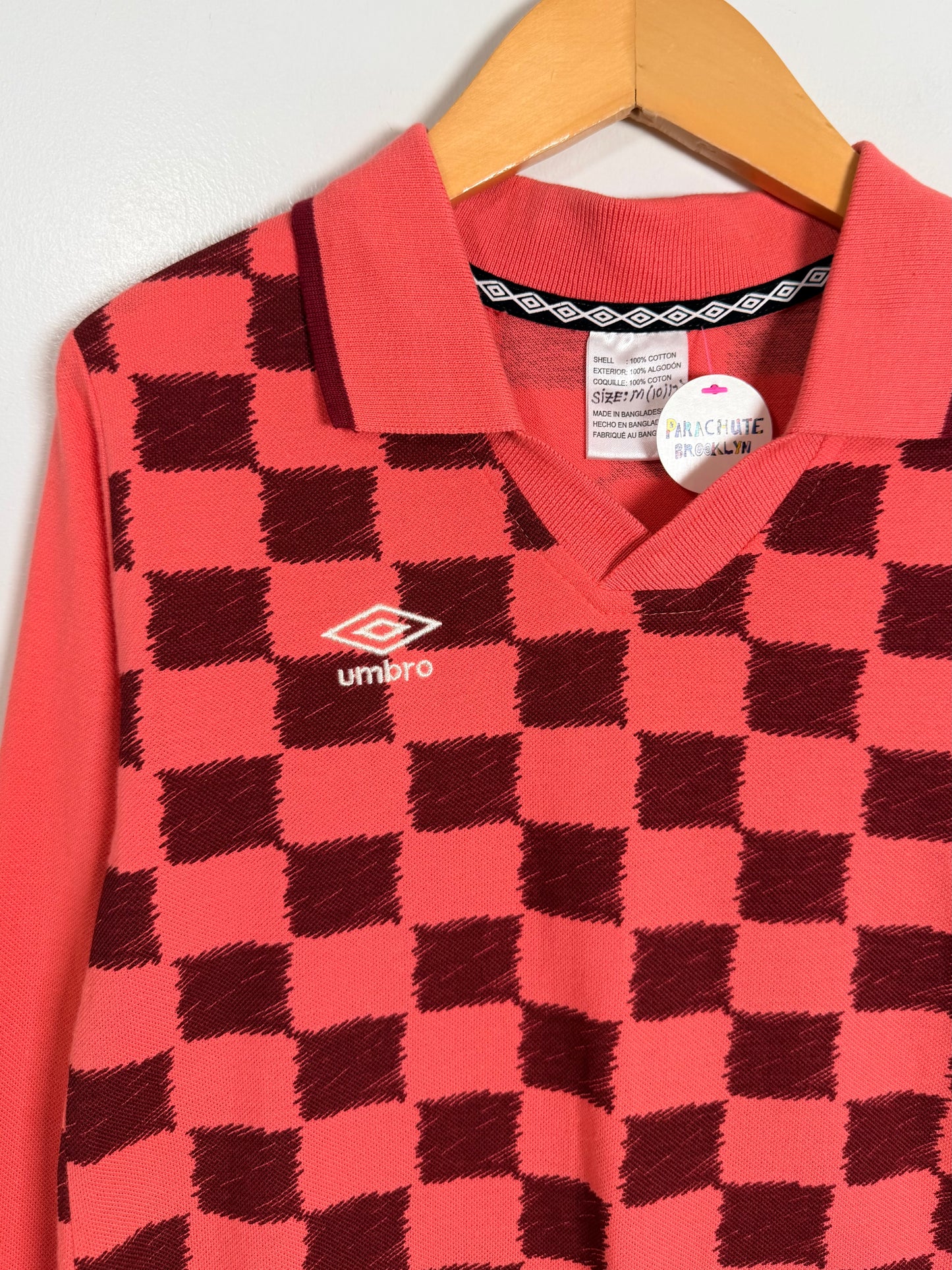 Red and black checkered polo shirt with Umbro logo on a hanger against a white background