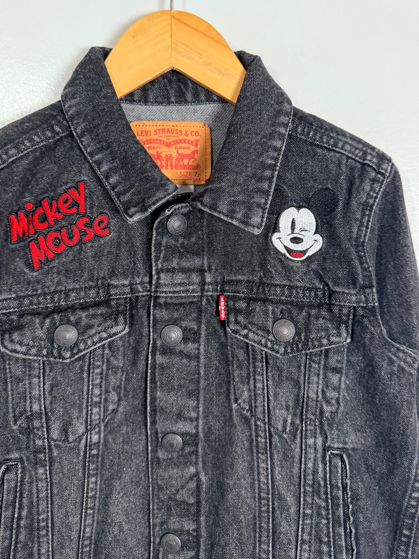 Black denim jacket with Mickey Mouse patch and Levi's logo on a hanger.