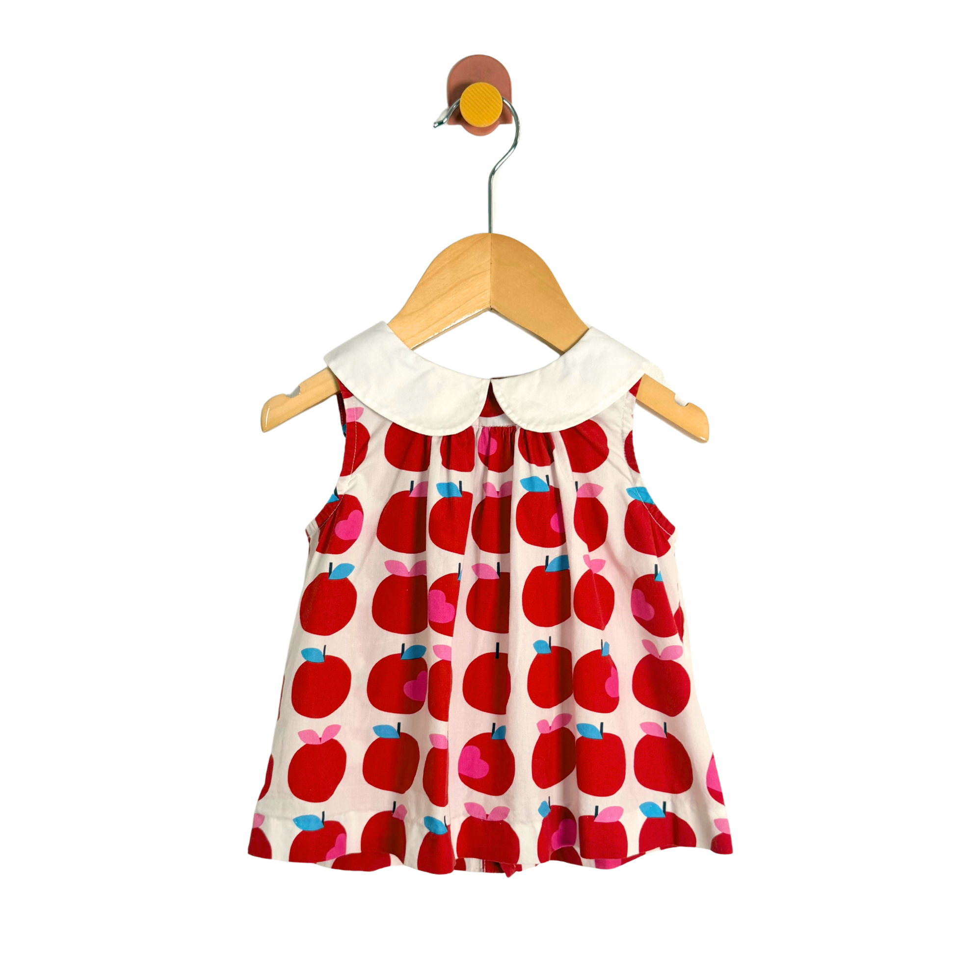 Children's dress with red apple pattern on a hanger against a white background