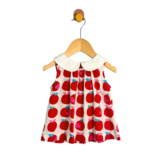 Children's dress with red apple pattern on a hanger against a white background