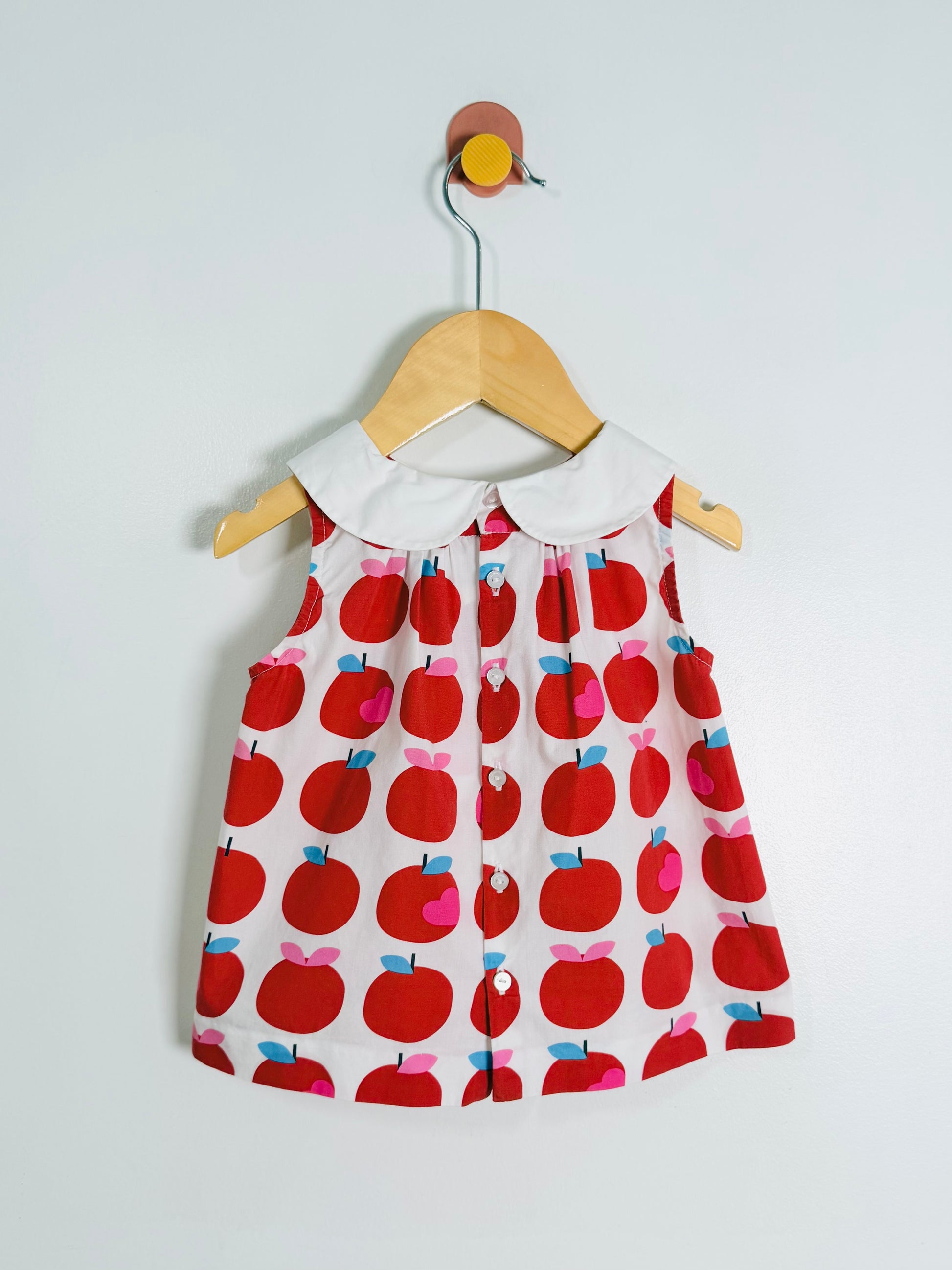 Children's dress with apple pattern on a hanger against a light gray background