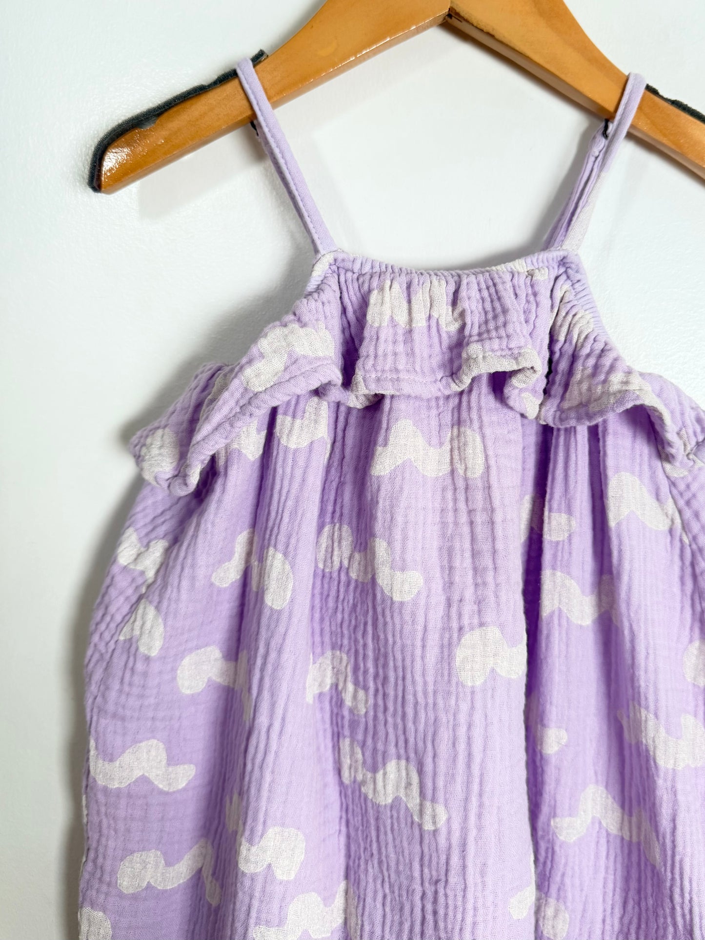Purple romper with white patterns on a wooden hanger against a white background