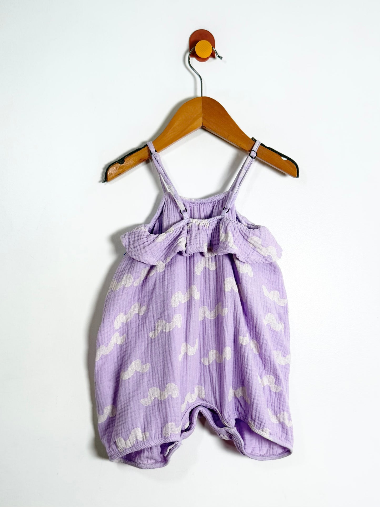 Purple baby romper with white cloud pattern on a wooden hanger against a white background