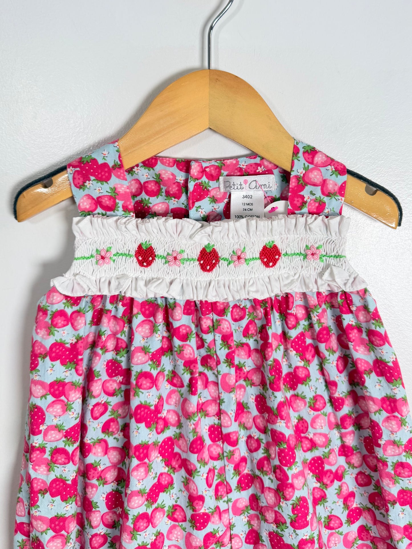 Children's dress with strawberry pattern on a hanger against a white background