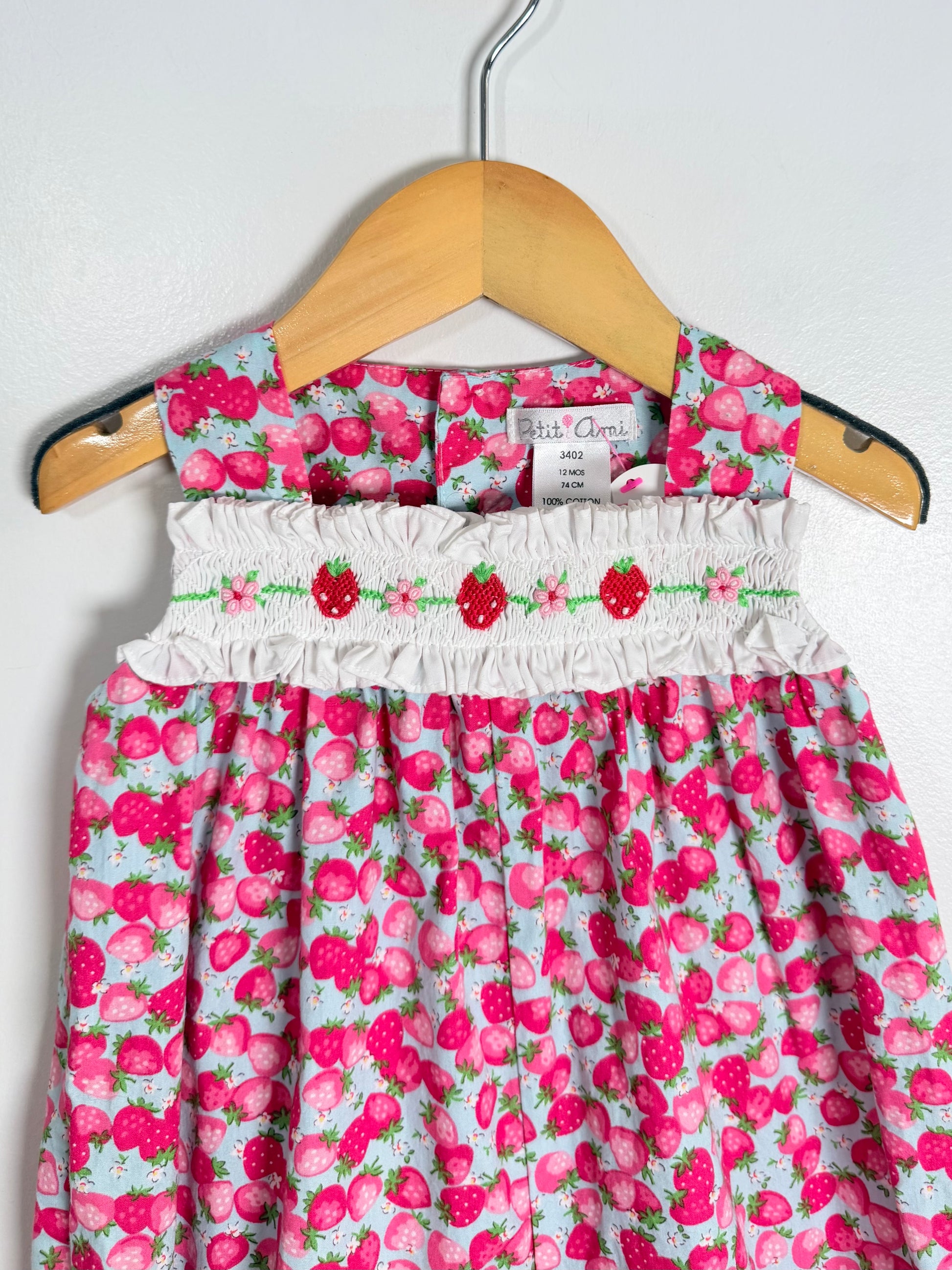 Children's dress with strawberry pattern on a hanger against a white background