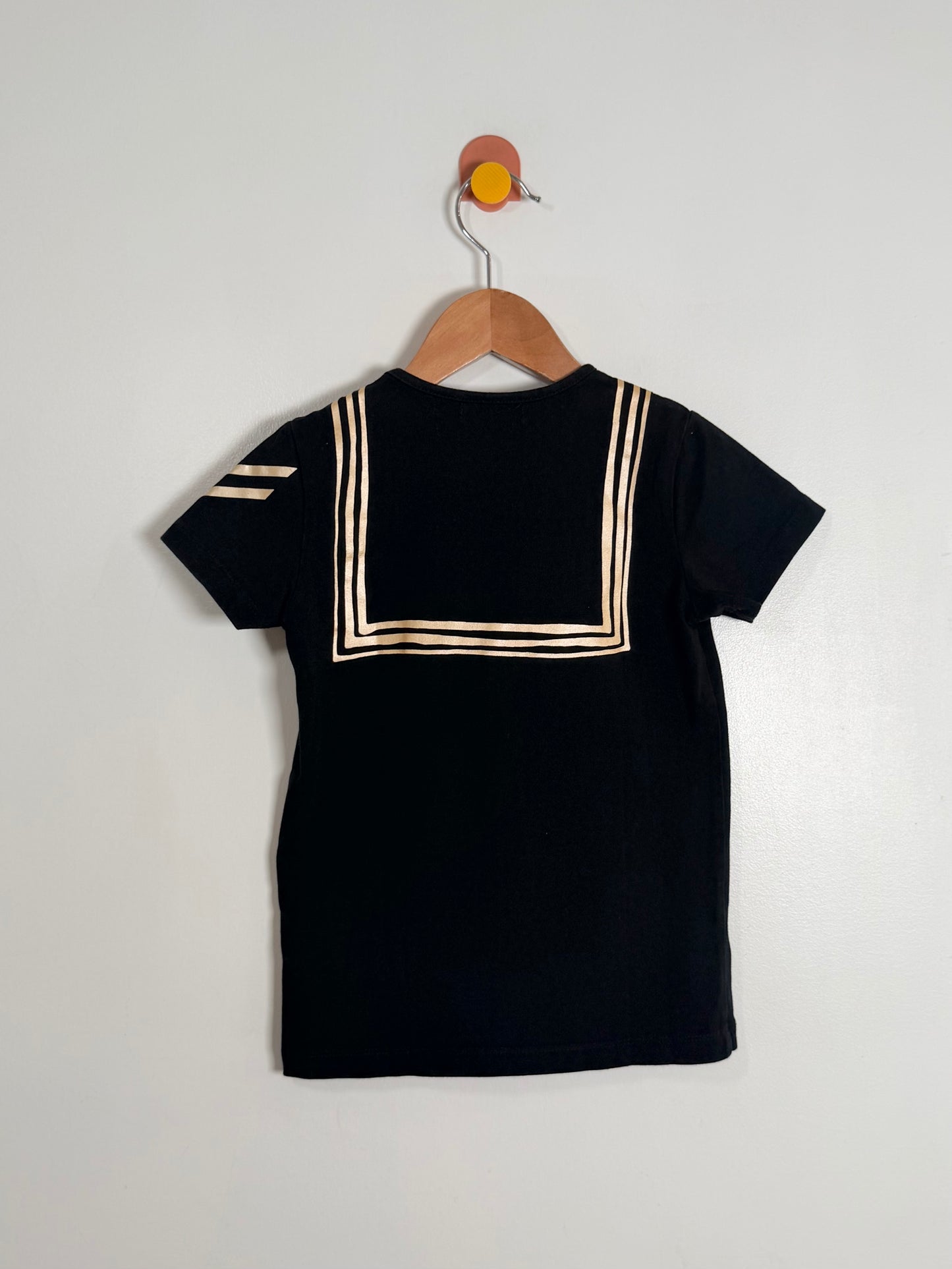 Black t-shirt with white trim on a wooden hanger against a light gray background