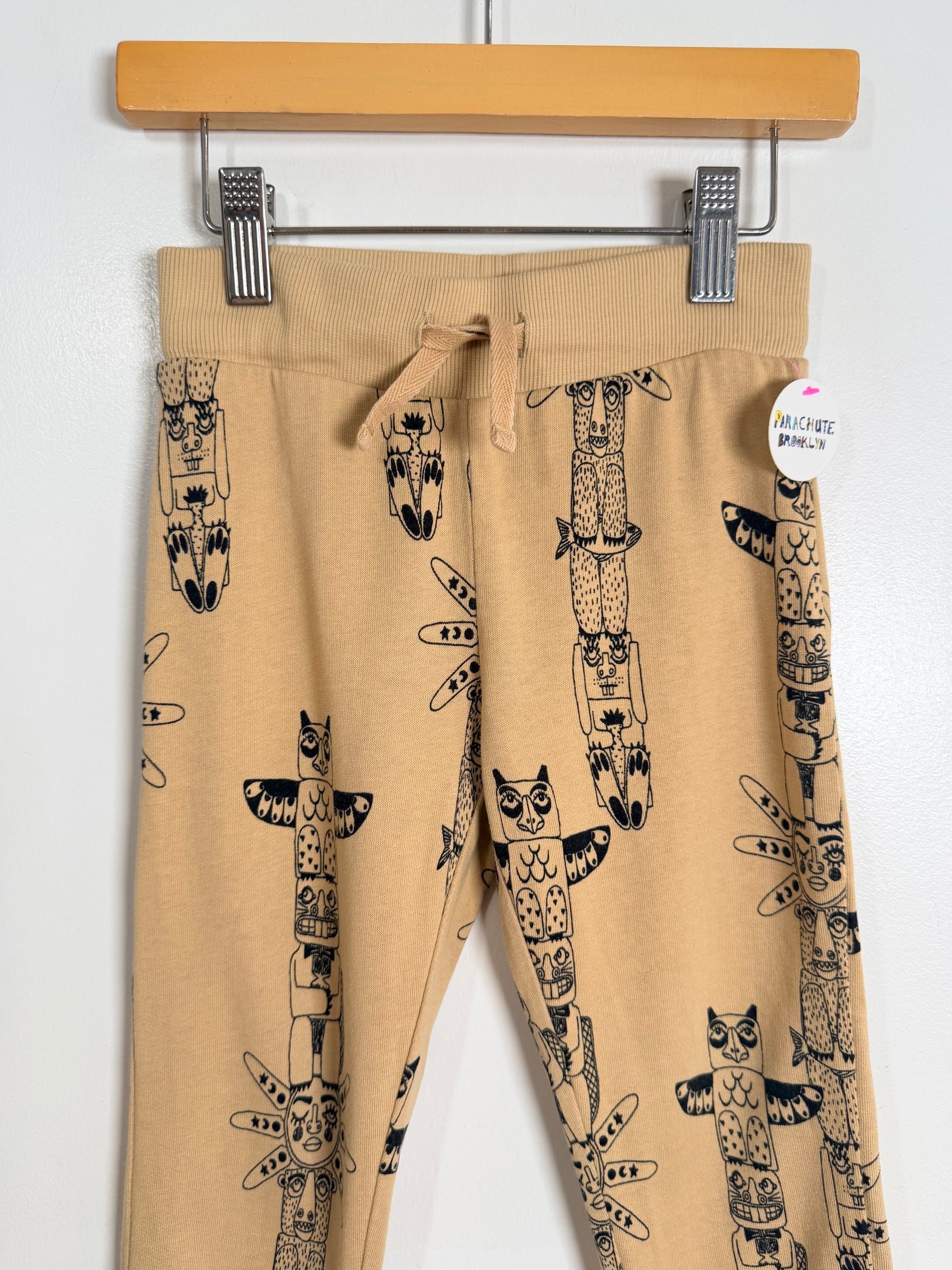 Beige sweatpants with black animal print hanging on a wooden hanger against a white background