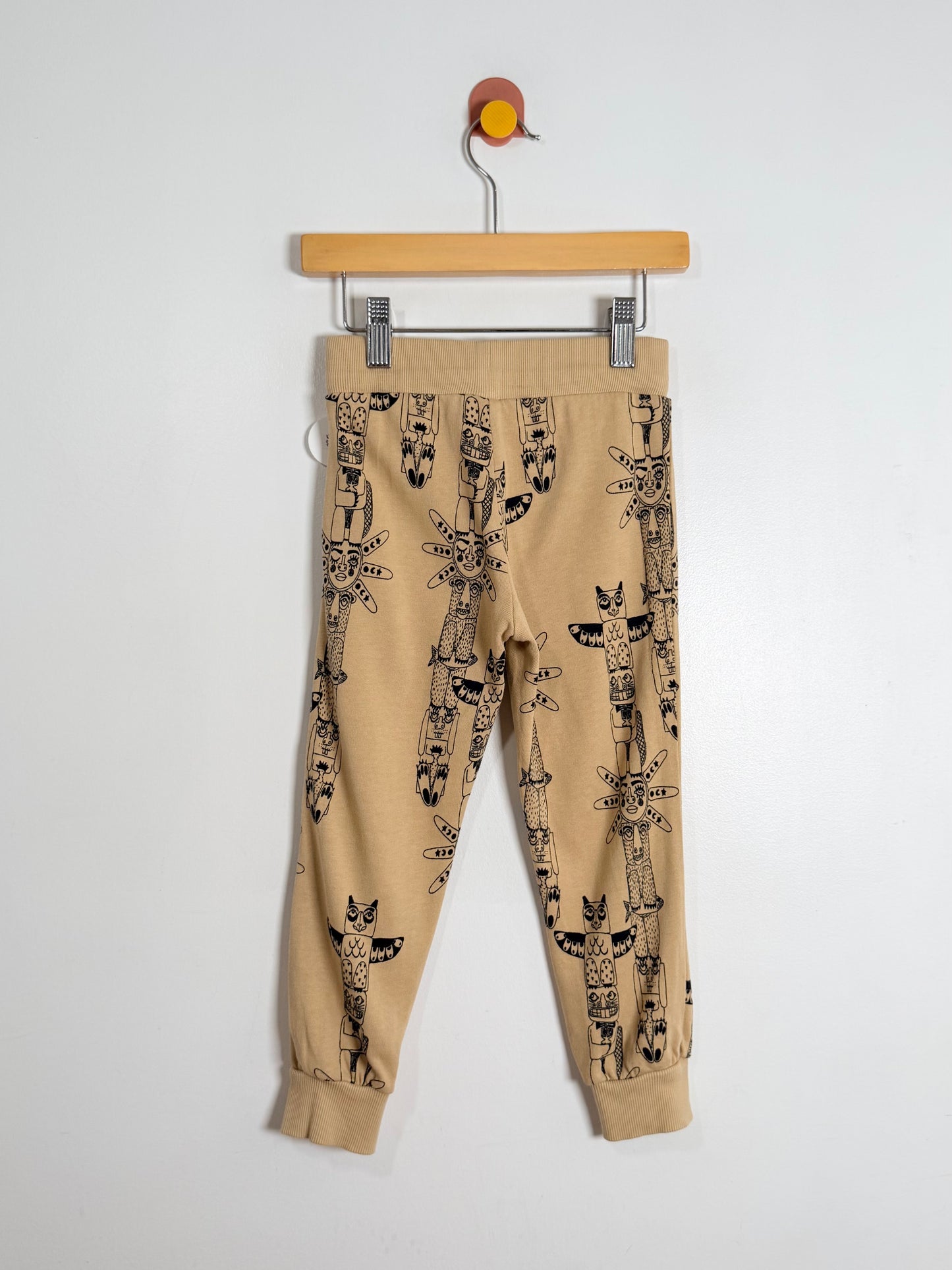 Beige pants with a pattern hanging on a wooden hanger against a white background