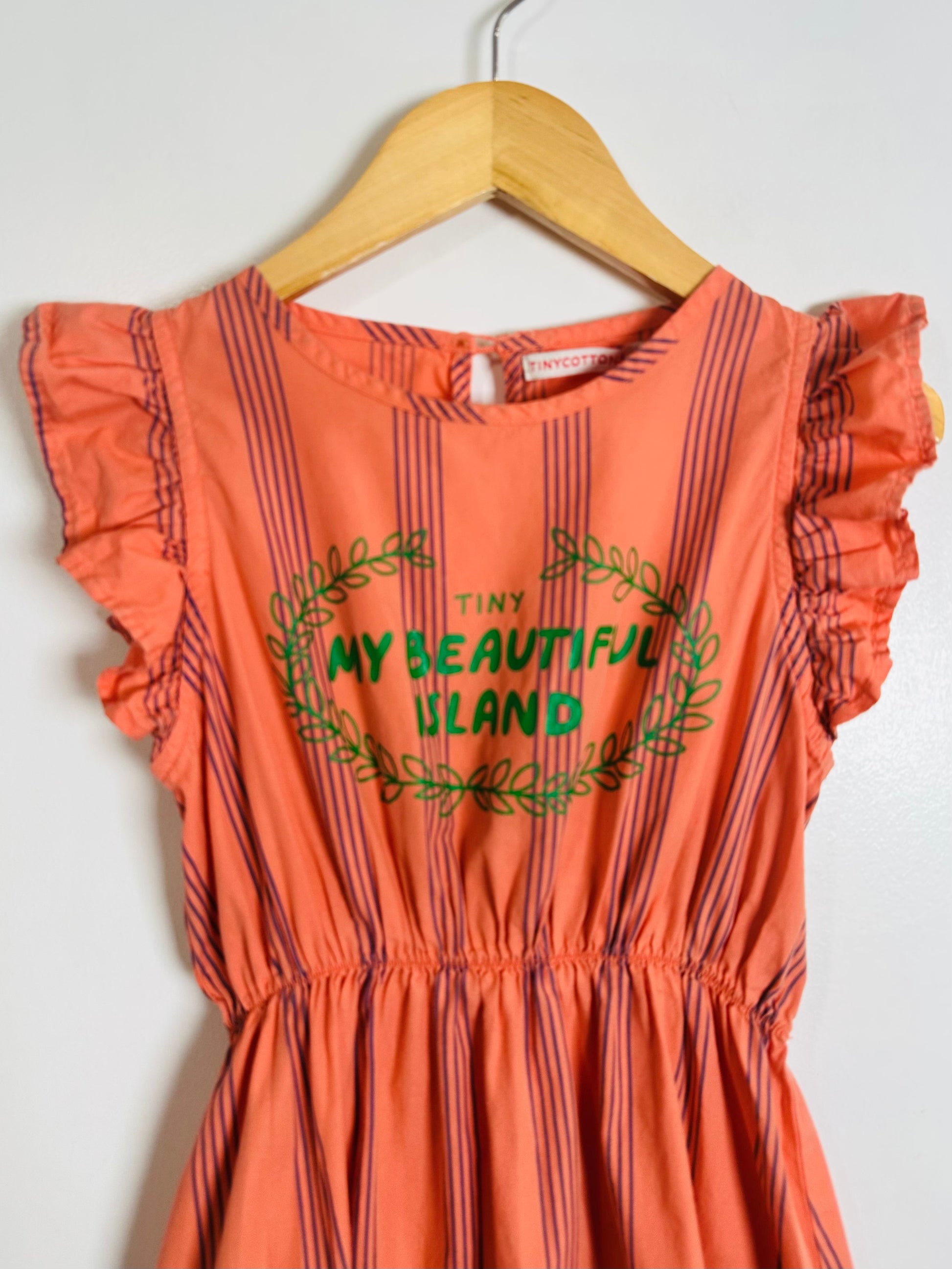 Orange dress with green text and leaf design on a hanger against a white background