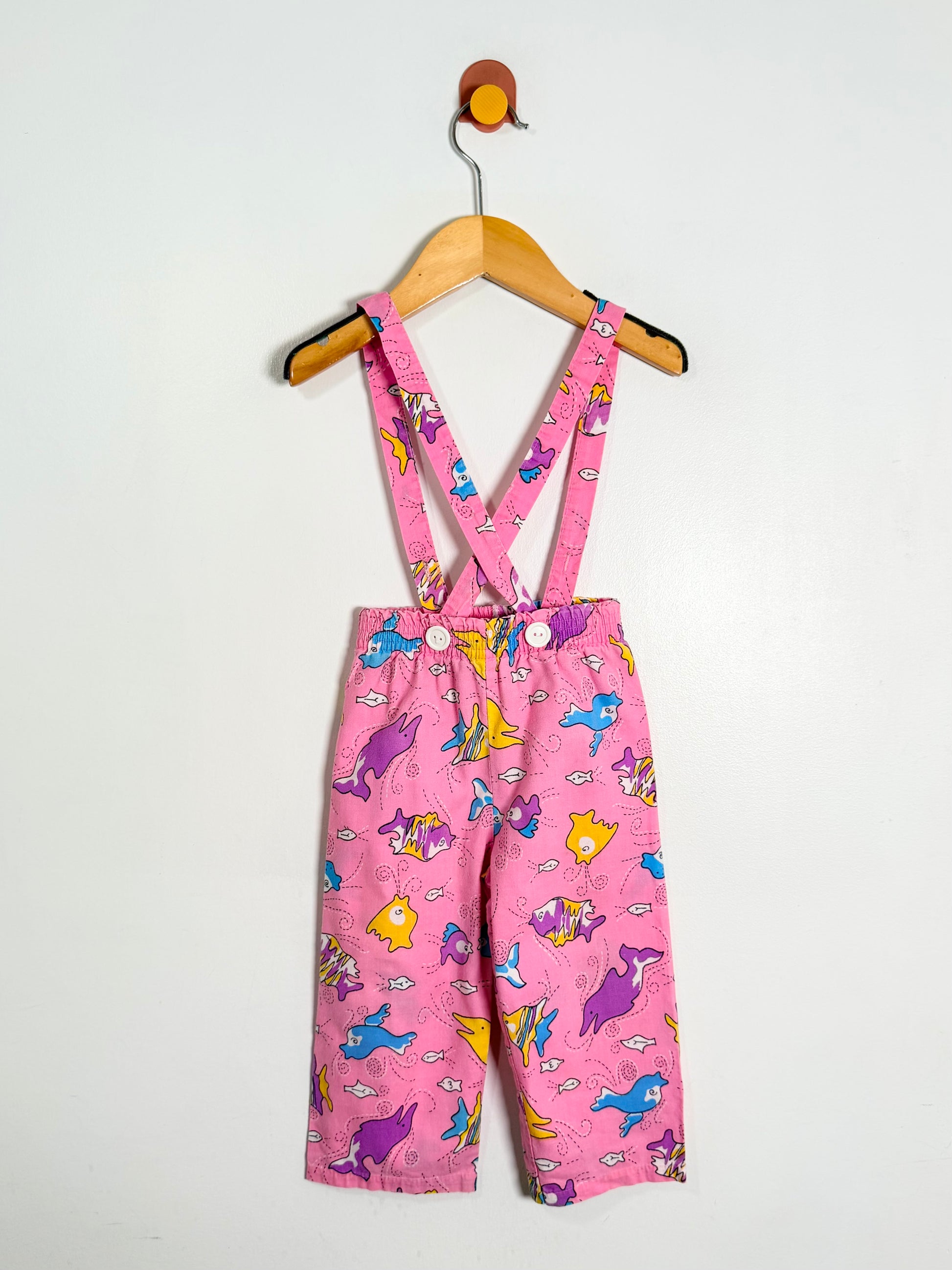 Pink children's overalls with cartoon designs on a white background