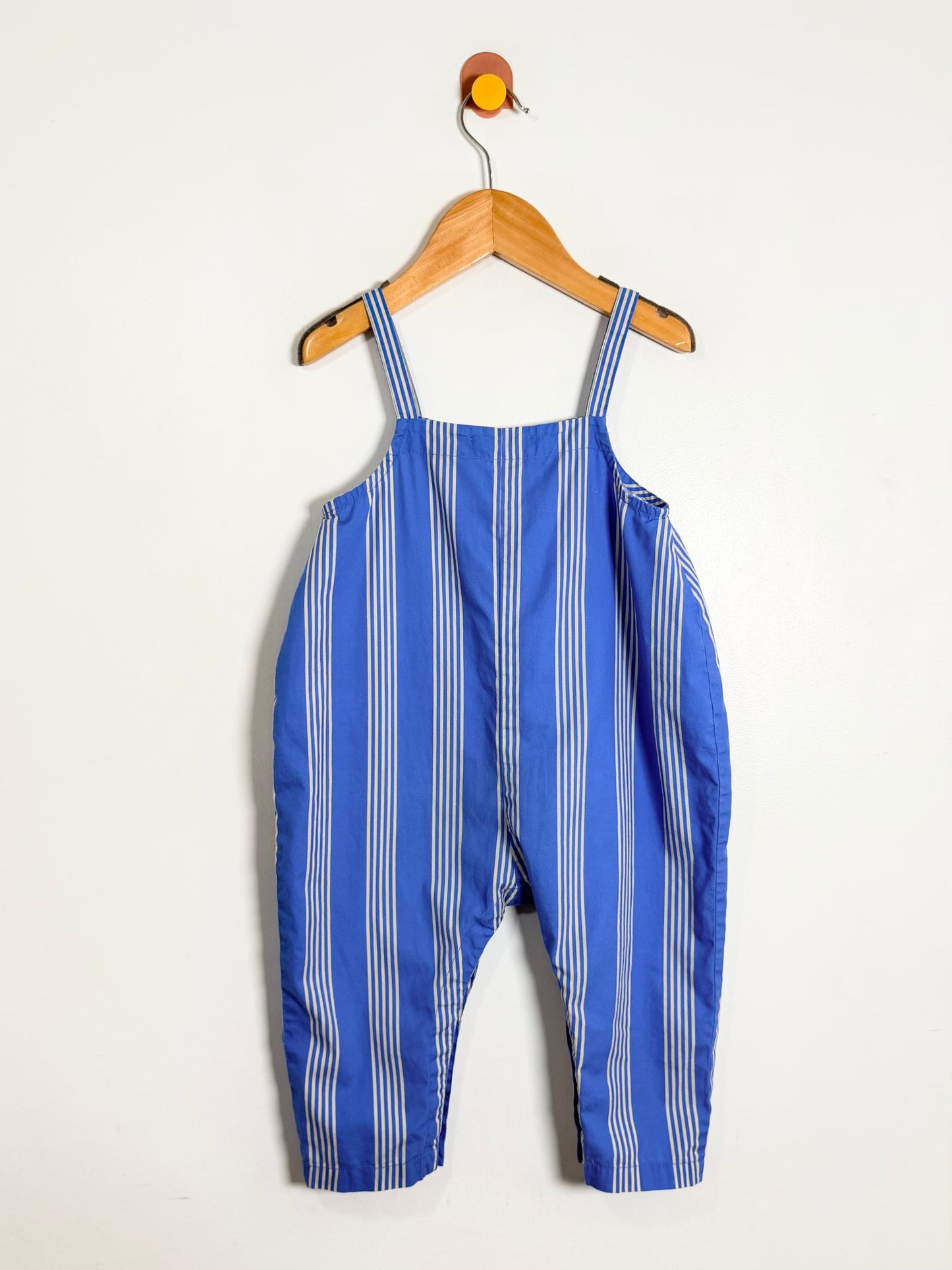 Blue and white striped overalls hanging on a wooden hanger against a white background