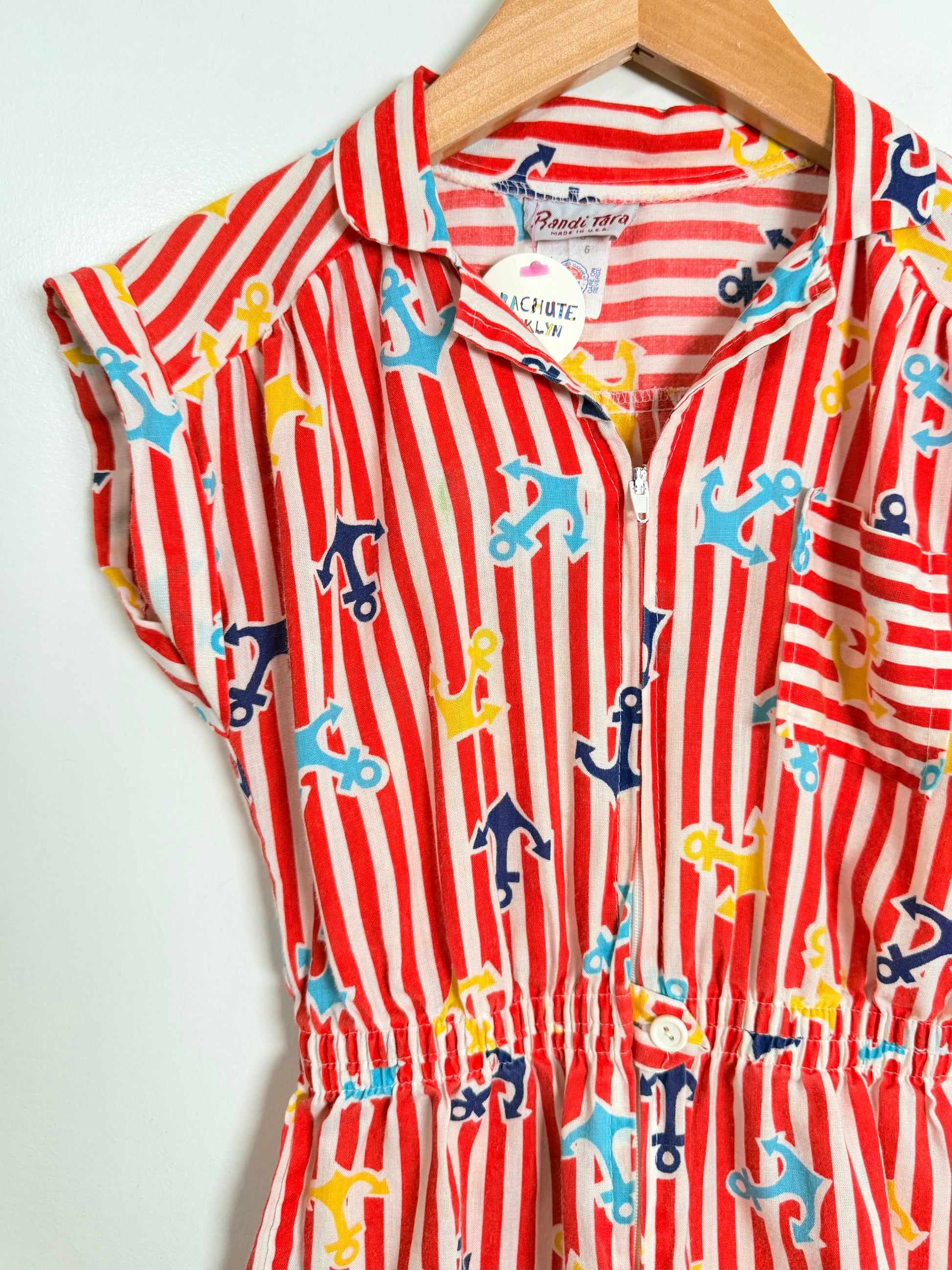 Red and white striped romper with blue and yellow anchors on a hanger against a white background