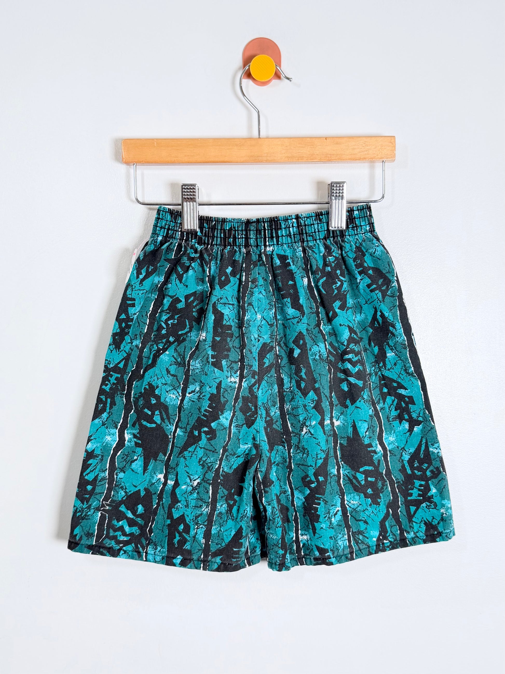 Teal and black patterned shorts on a hanger against a white background