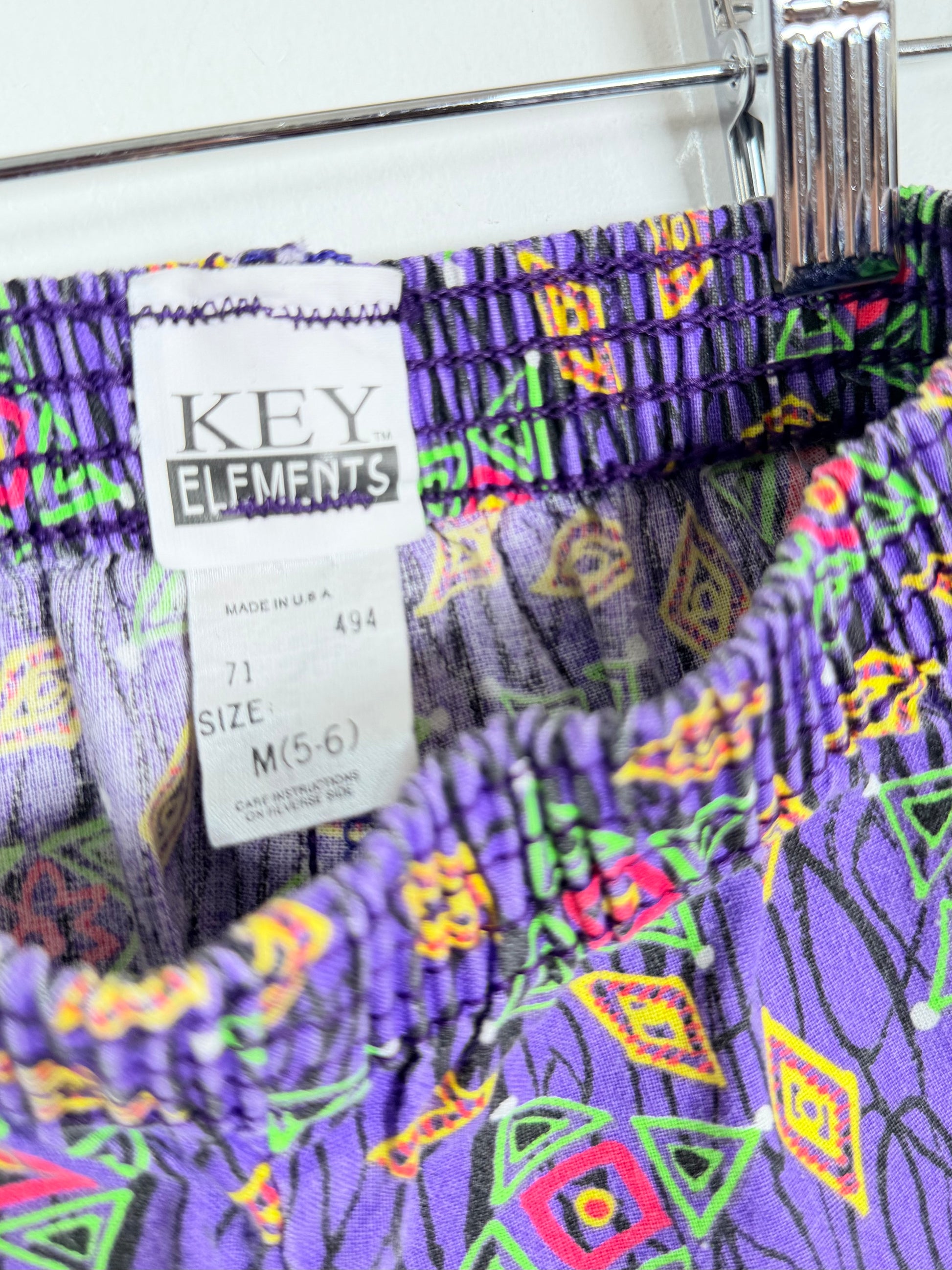 Colorful patterned pants with a 'Key Elements' tag on a rack.