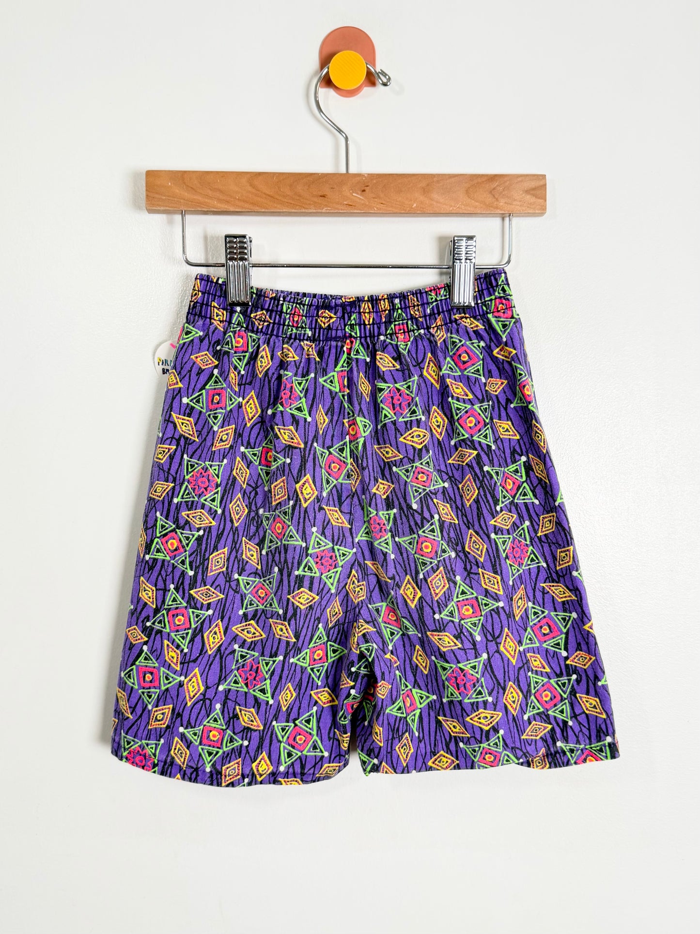 Purple shorts with colorful geometric pattern on a hanger against a white background