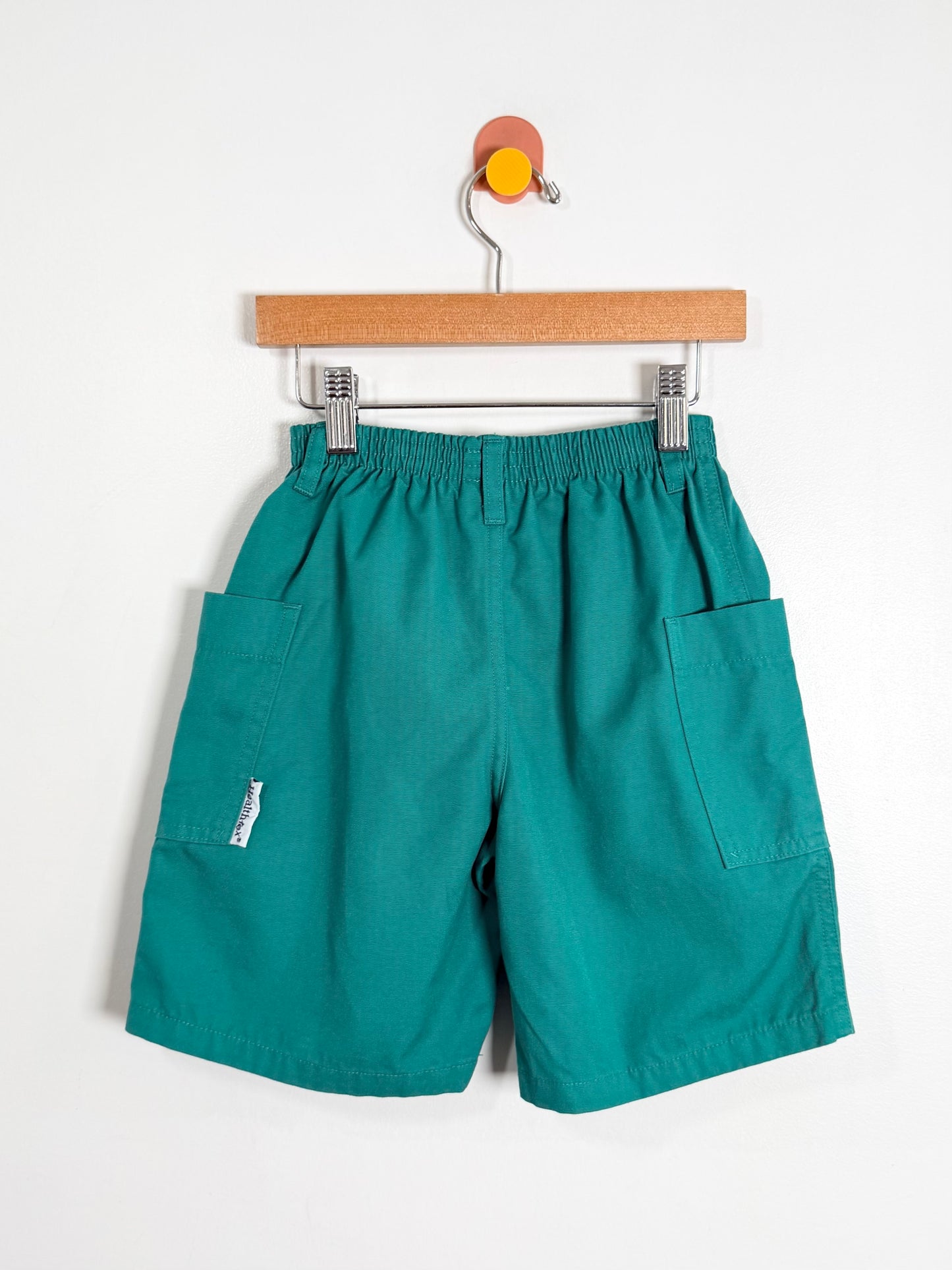 Teal shorts on a hanger against a white background