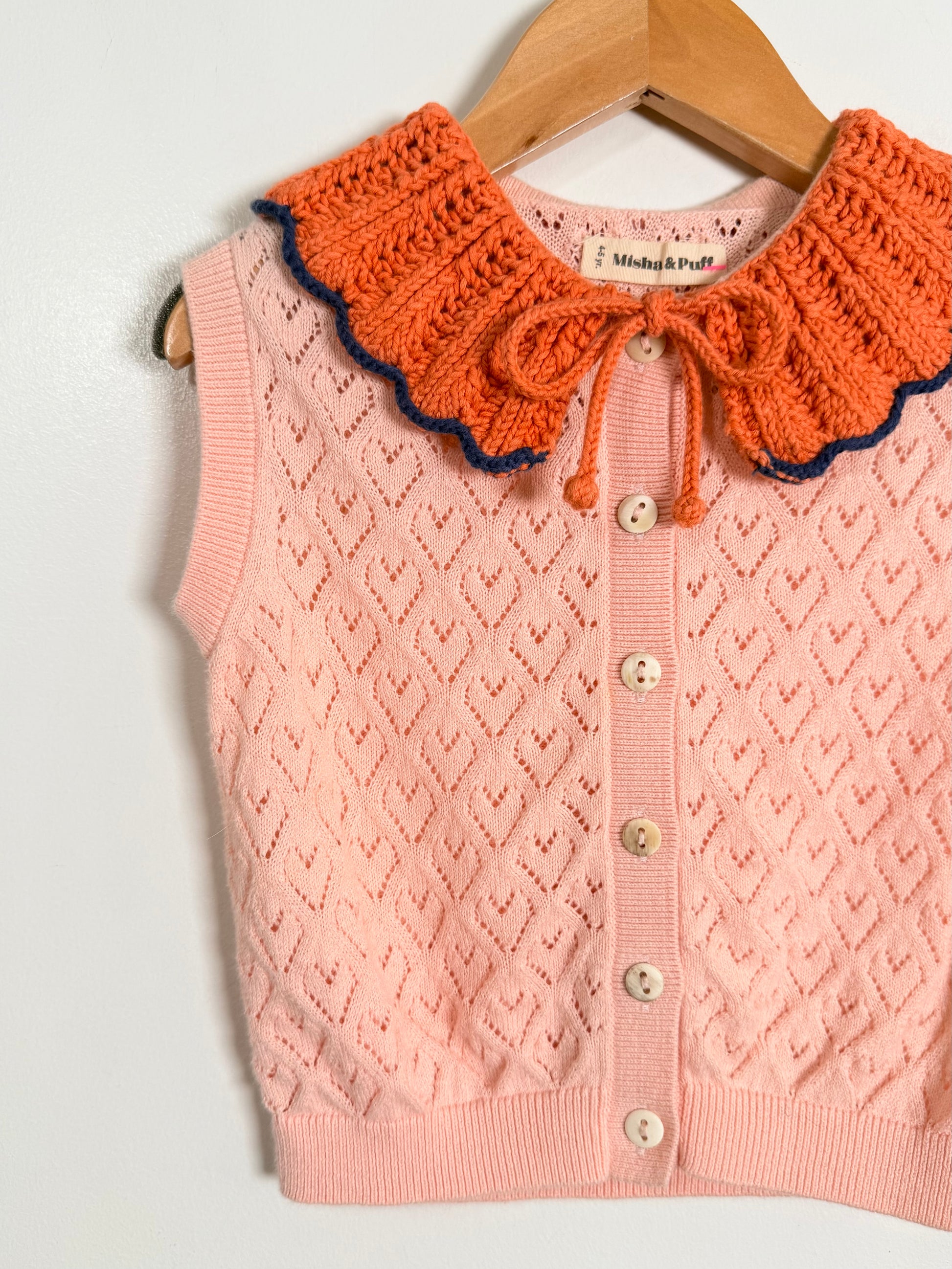 Pink cardigan with orange knit collar on a wooden hanger against a white background