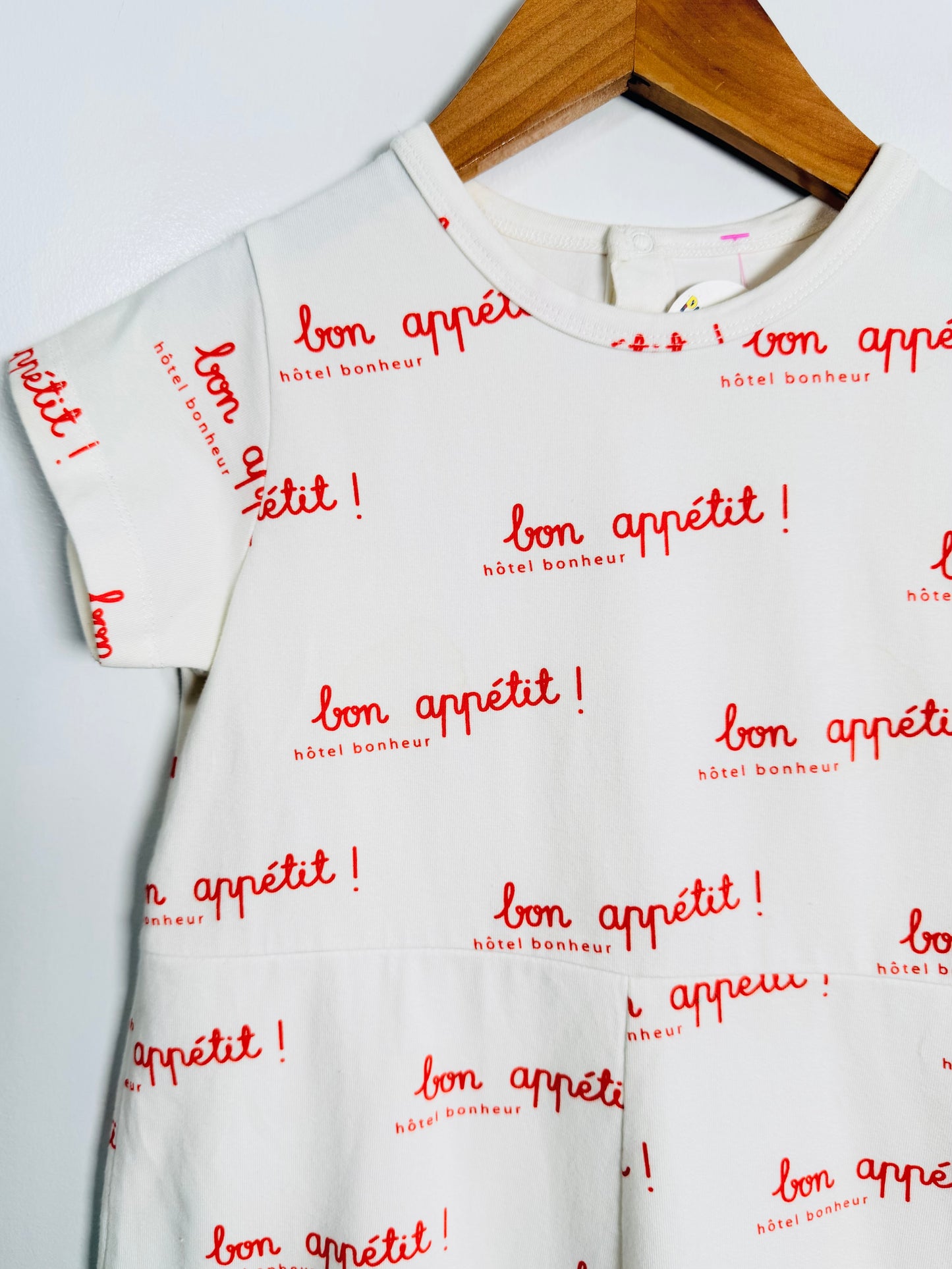 White t-shirt with red 'bon appétit!' text on a wooden hanger against a white background