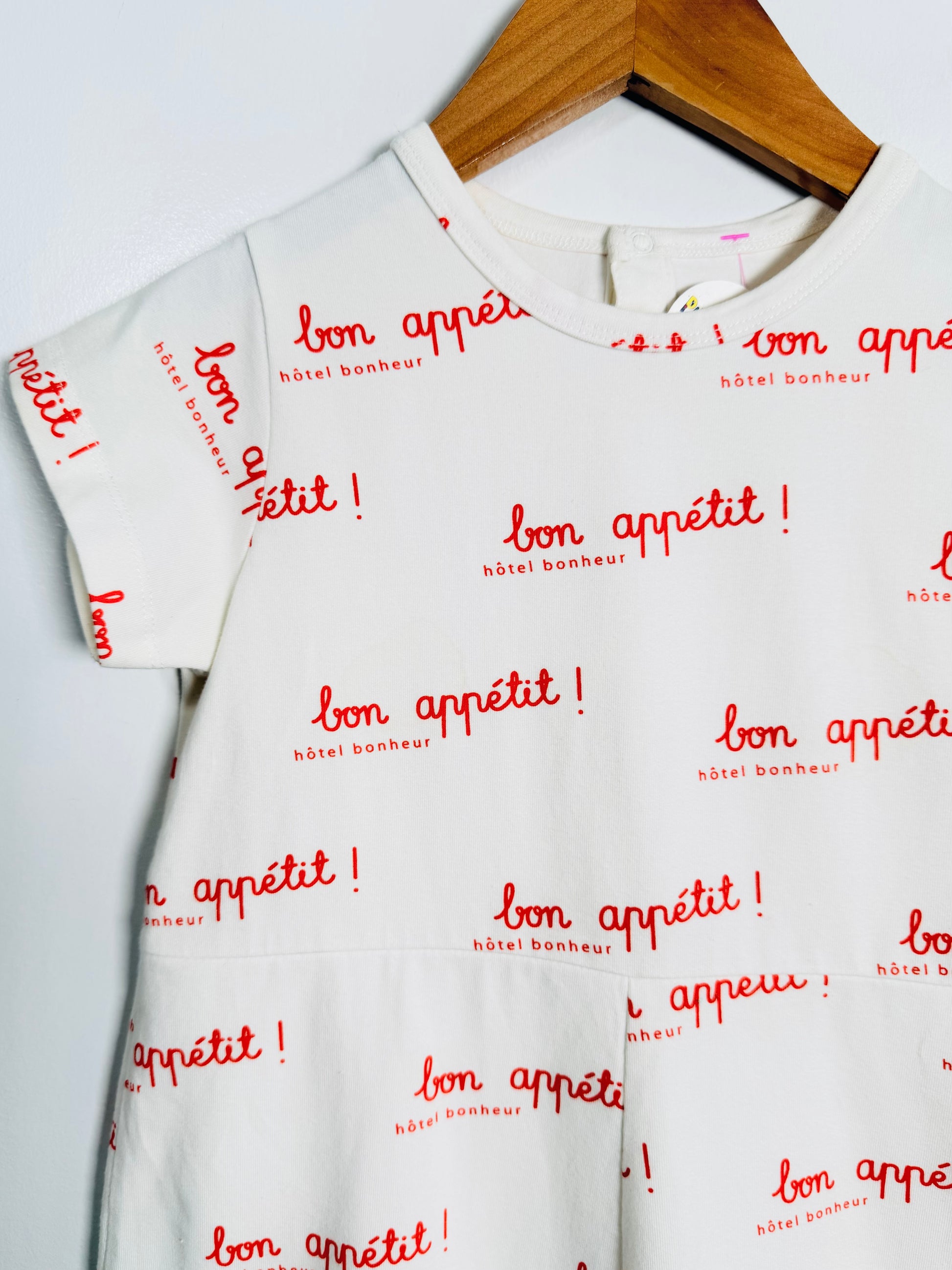 White t-shirt with red 'bon appétit!' text on a wooden hanger against a white background