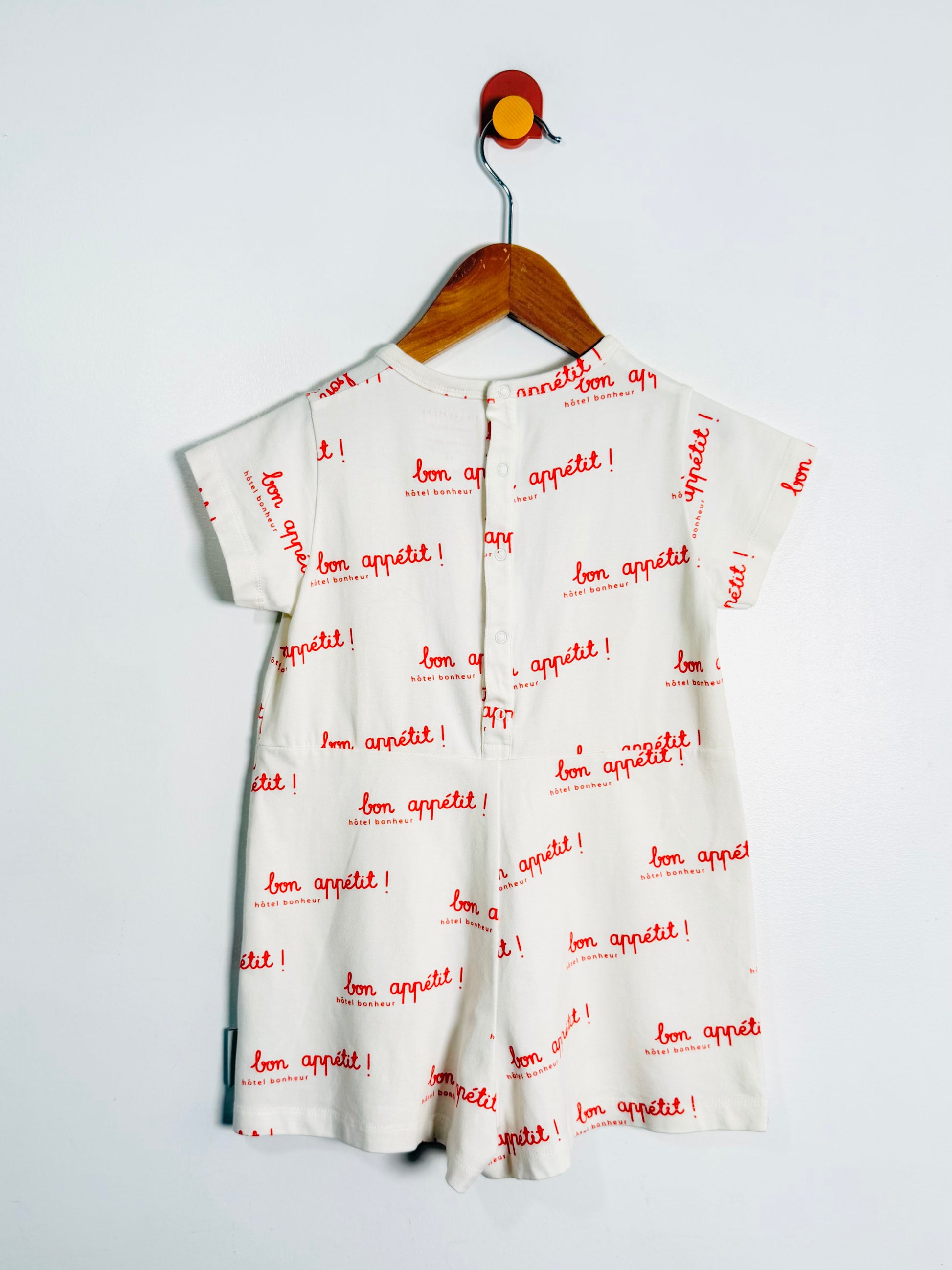 White dress with red text 'bon appetit!' on a hanger against a light gray background