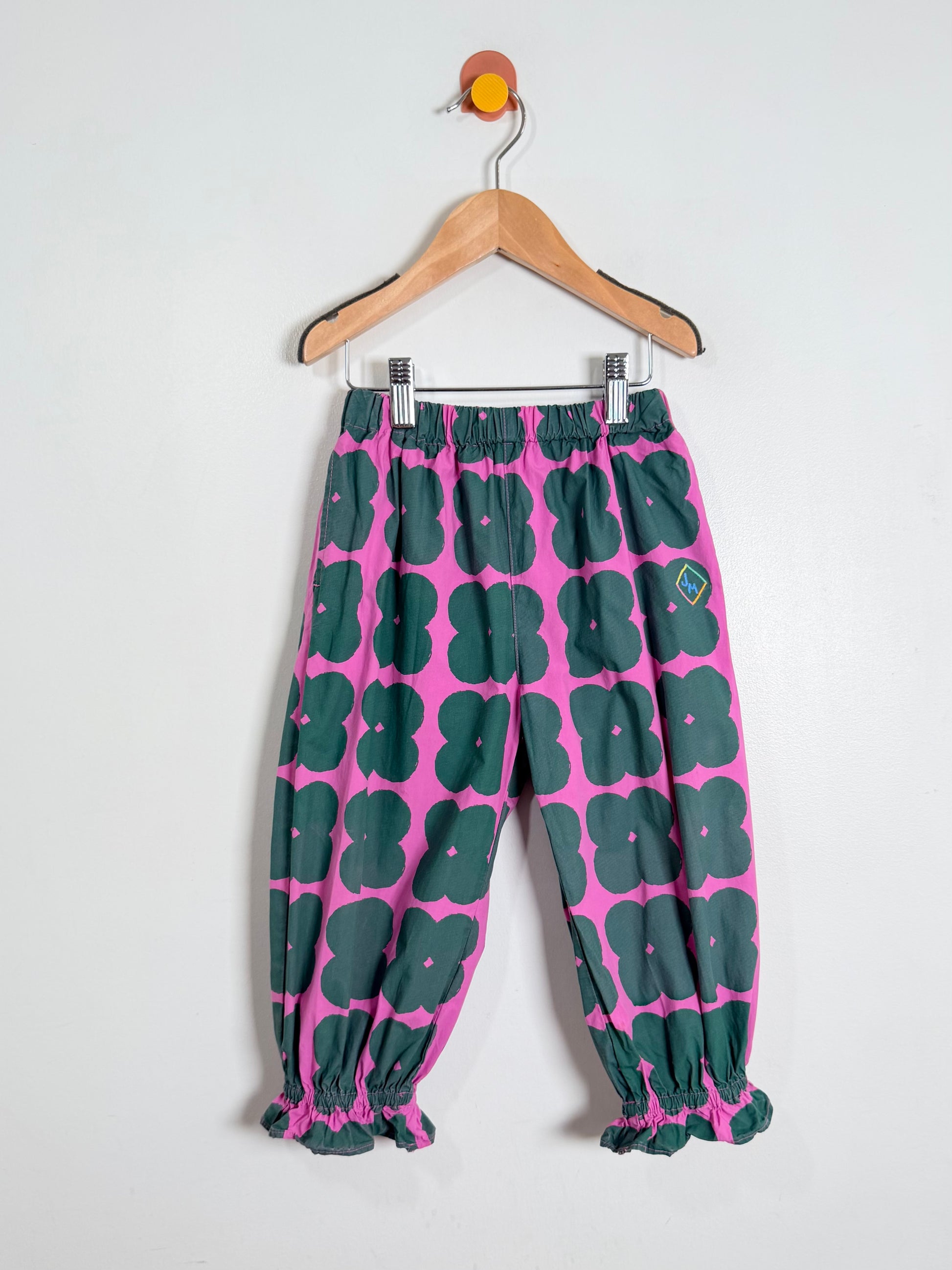Pink and green patterned pants on a hanger against a white background