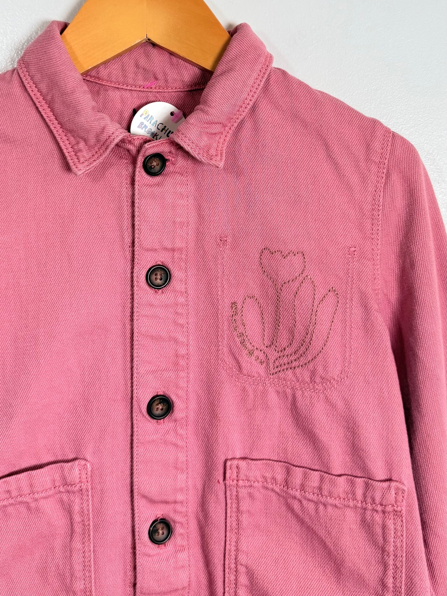 Pink jacket with floral embroidery on a hanger against a white background
