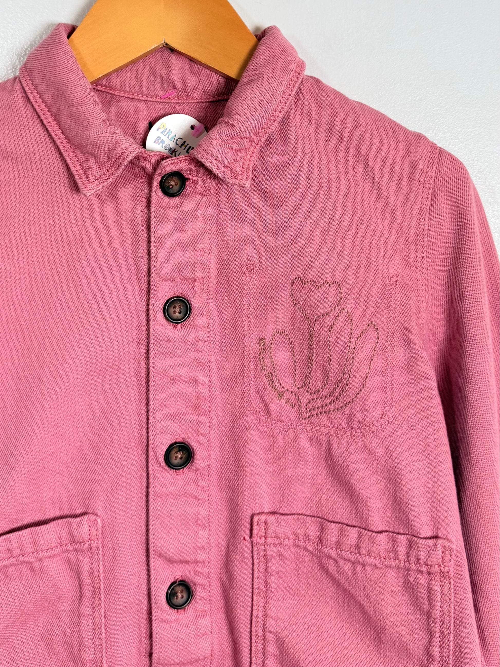 Pink jacket with floral embroidery on a hanger against a white background