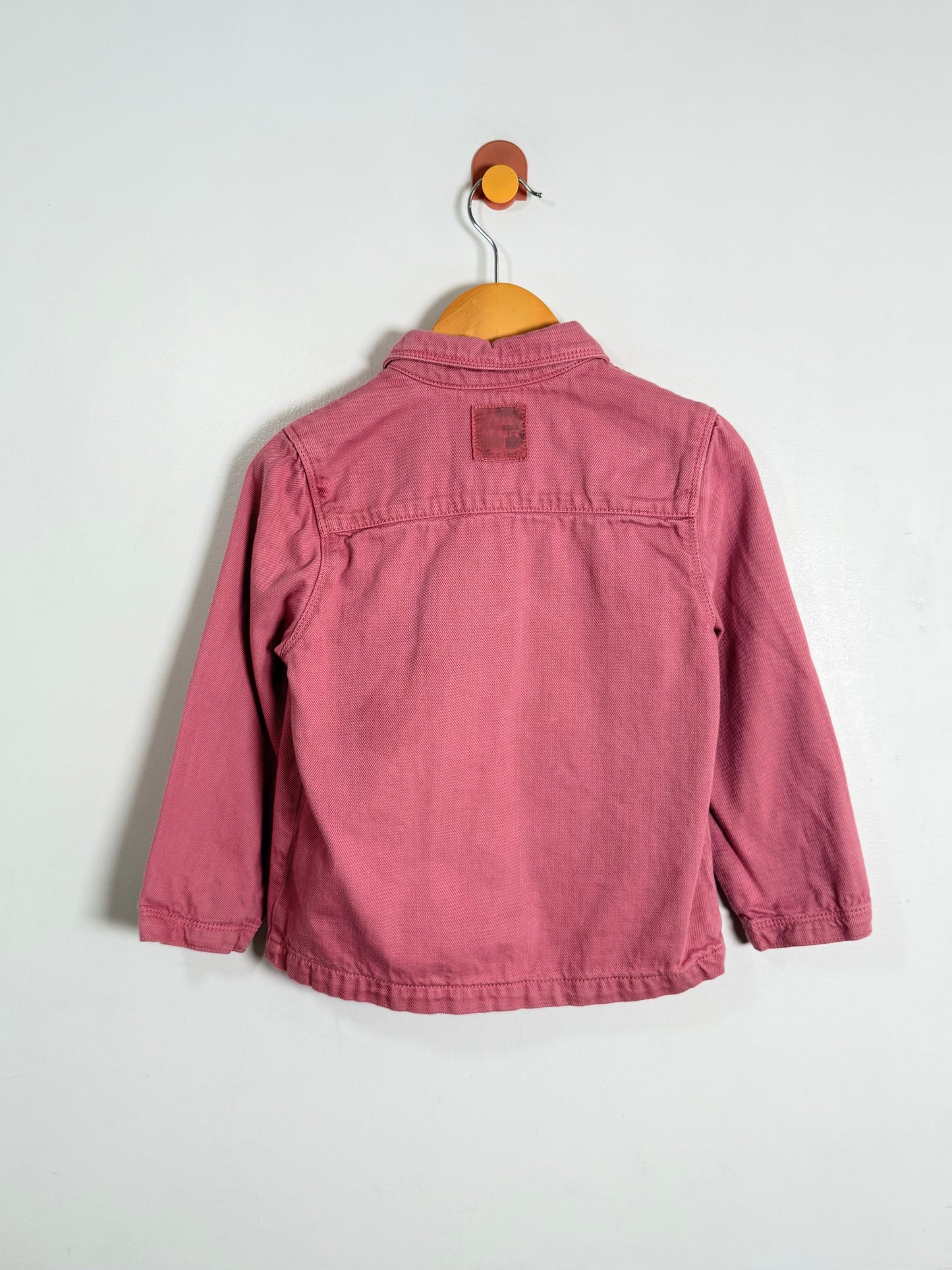 Pink jacket on a wooden hanger against a white background