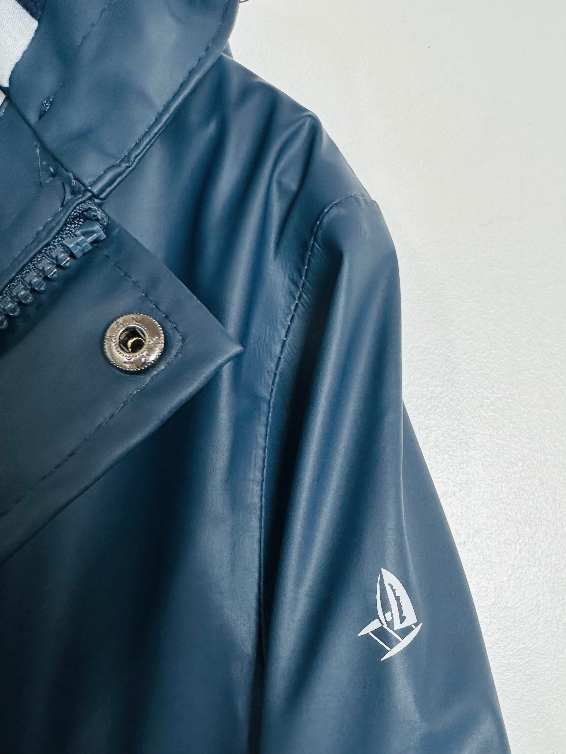 Close-up of a blue raincoat with a brand logo on a light gray background