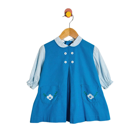 Blue dress with floral pockets on a wooden hanger against a white background