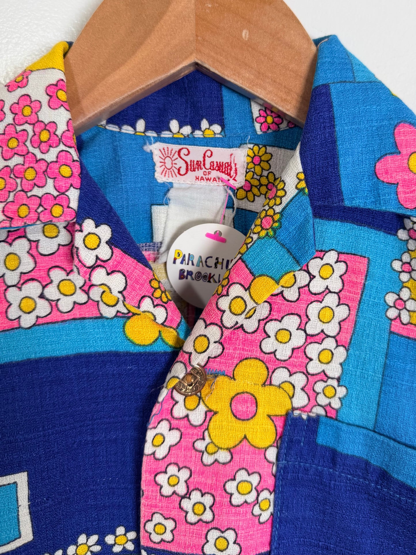 Colorful floral-patterned shirt with a wooden hanger on a white background