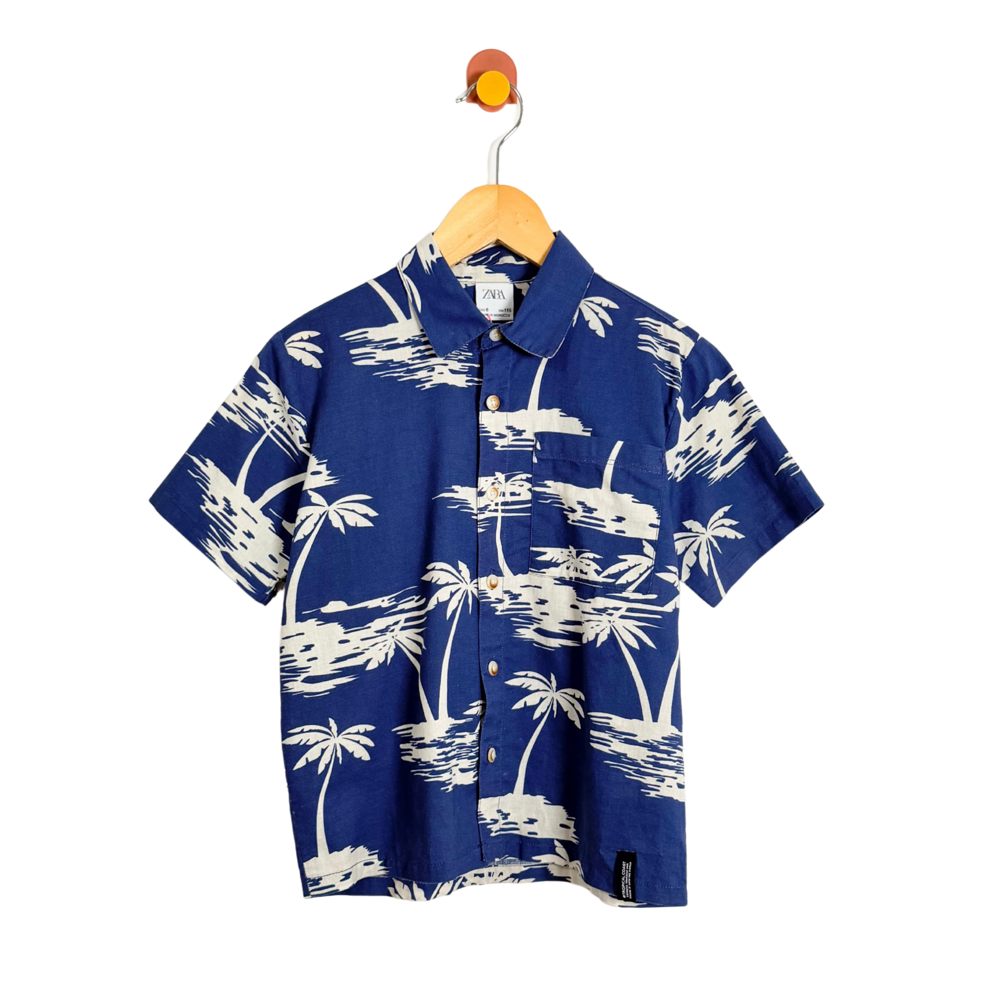 Blue shirt with white palm tree pattern on a hanger against a white background