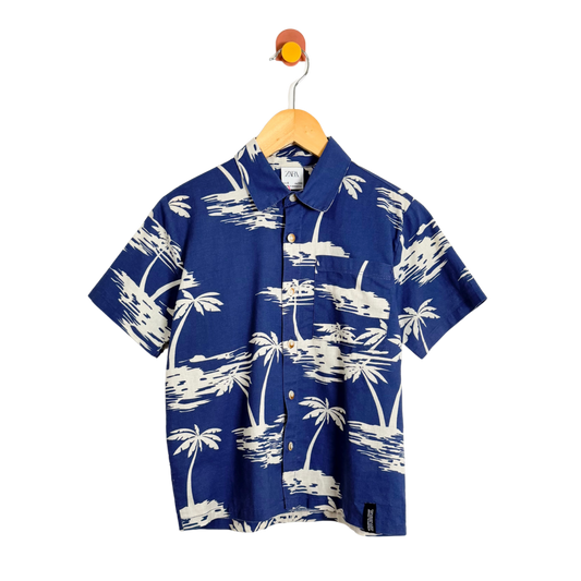 Blue shirt with white palm tree pattern on a hanger against a white background