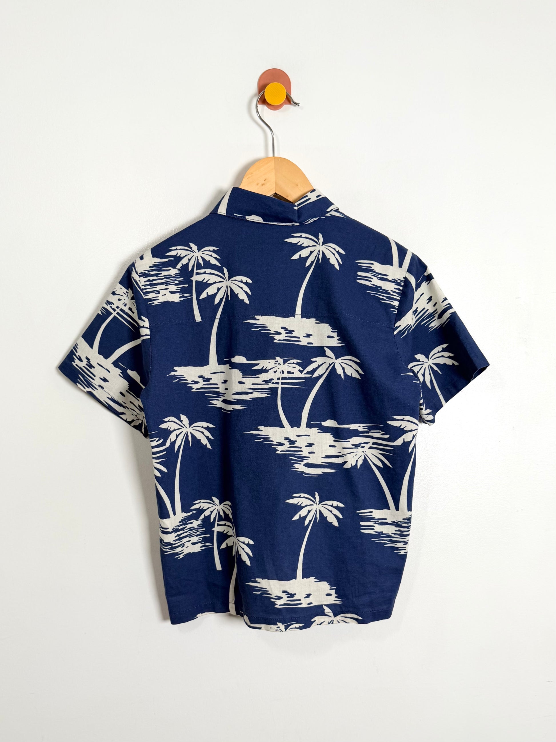 Navy blue shirt with white palm tree pattern on a hanger against a white background